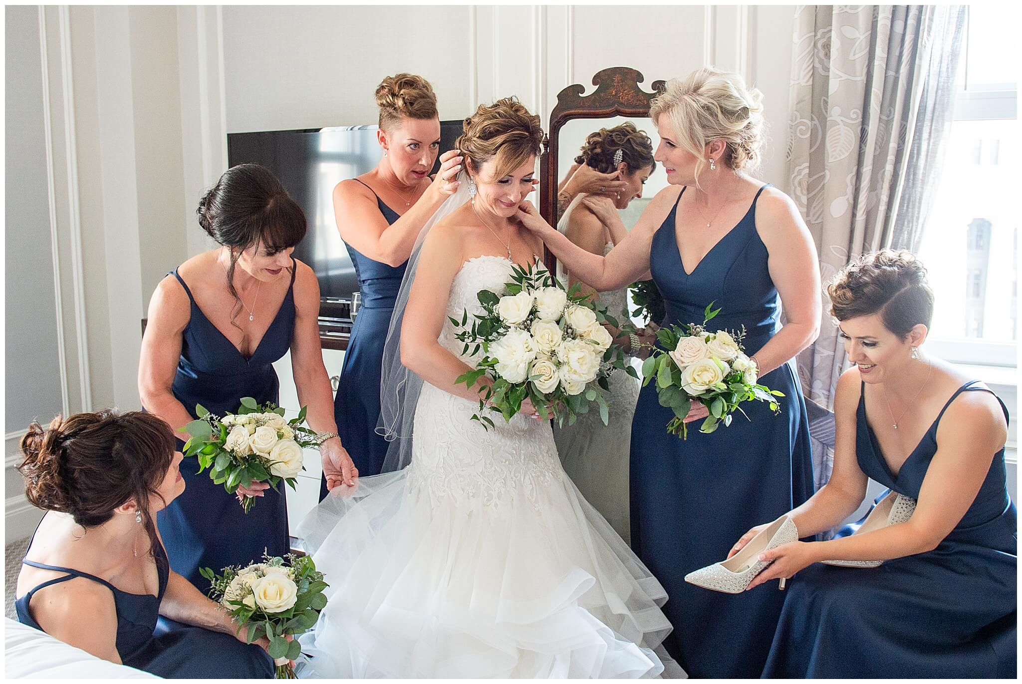 a bride is assisted for her Chateau Laurier wedding by her bridesmaids in navy dresses 