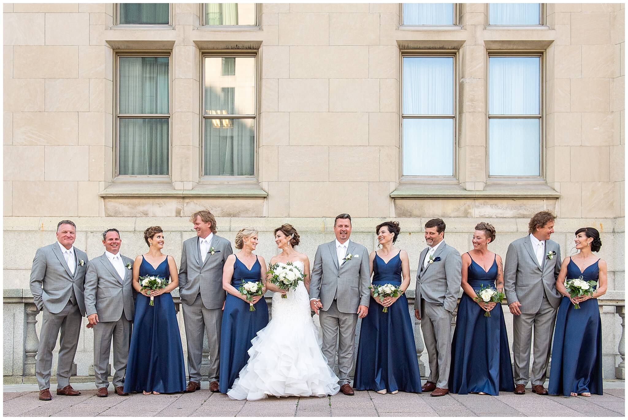 a bride and groom with their bridesmaids in navy dresses and their groomsmen in grey suits.  Taken outside of the Chateau Laurier wedding venue