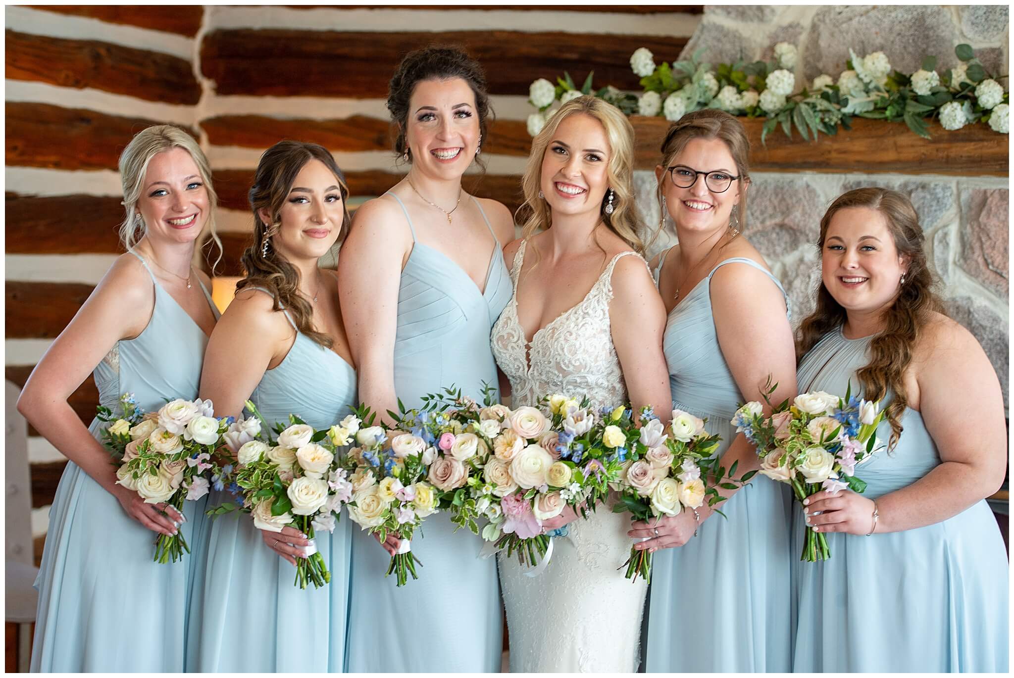  a bride and her bridesmaids in light blue gowns smiling and holding bouquets in the Stonefields Estate Farmhouse