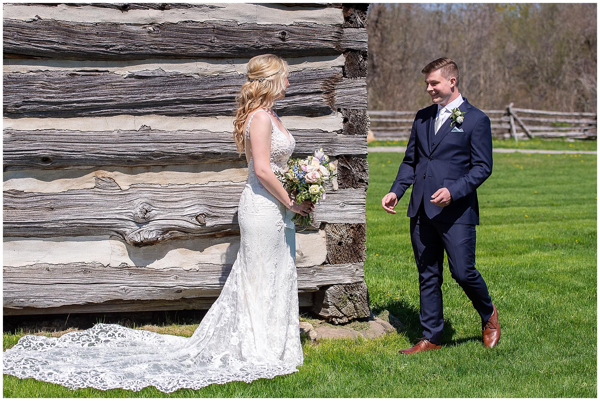 a groom in a navy blue suit smiling happily as he sees his bride for the first time at their Stonefields Estate wedding in Ottawa