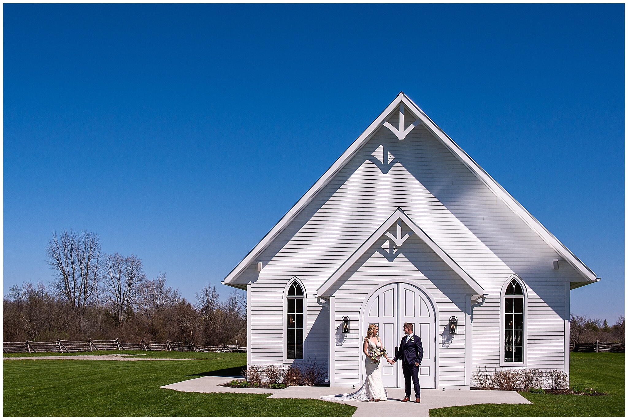 a bride and groom holding hands outside the Stonefields Estate Ceremony house with a big blue sky in the background. Captured by JEMMAN Photography