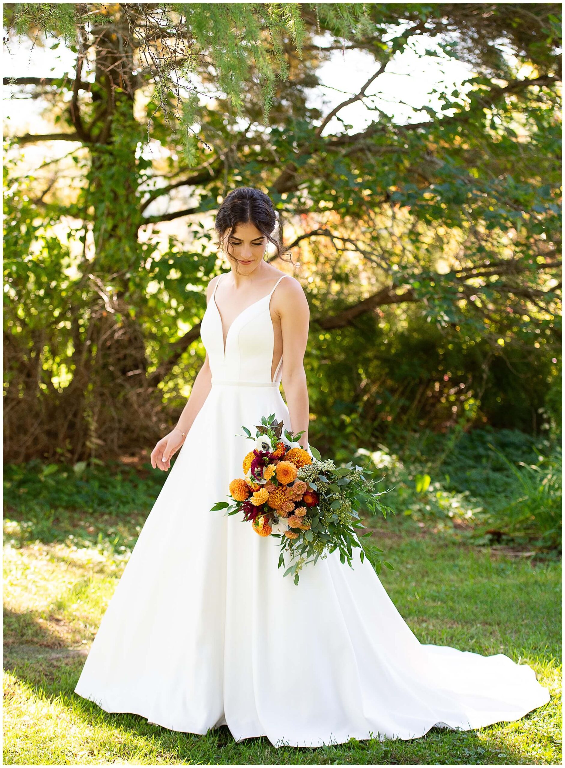 full length portrait of a bride in her wedding gown holding a fall coloured bouquet. Taken outdoors in the Heritage Garden of Strathmere wedding venue in Ottawa