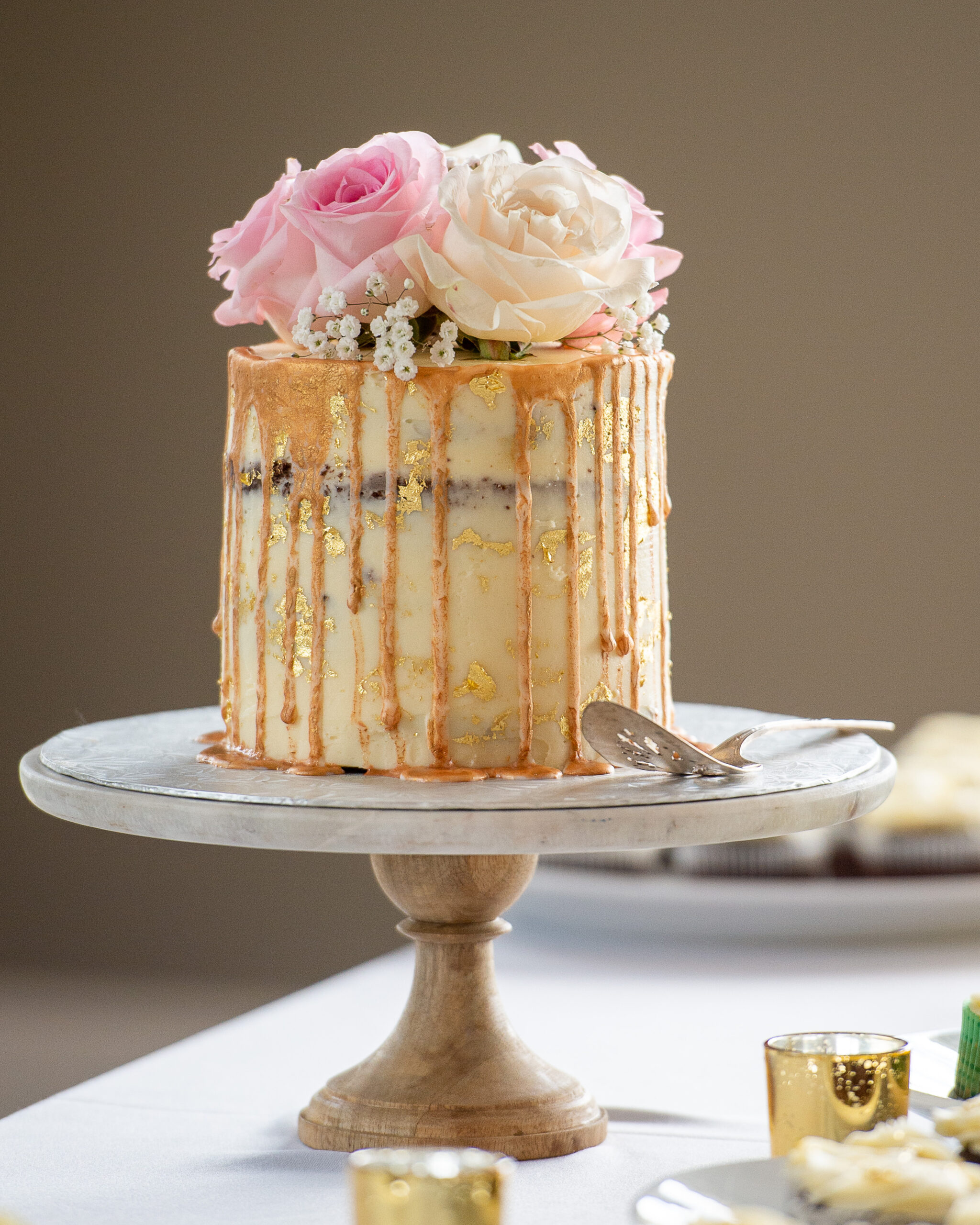 A closeup photo of a naked wedding cake topped with golden drizzle and fresh flowers. Captured by Ottawa Wedding Photographer JEMMAN Photography
