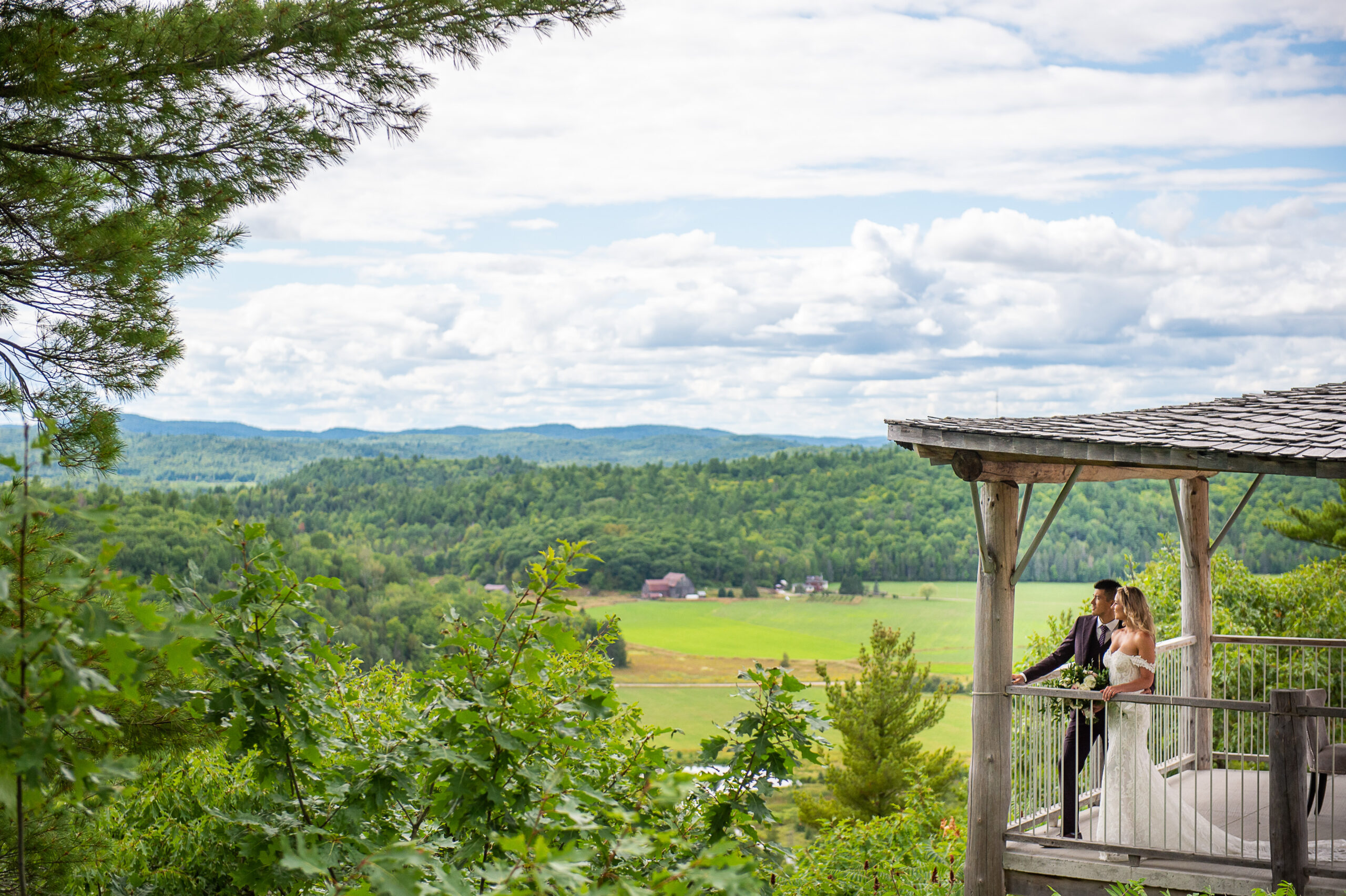 a scenic portrait showing a bride and groom looking out at the rolling hills and farmland of the Gatineau Hills. Captured on location at Le Belvedere weddings by JEMMAN Photography
