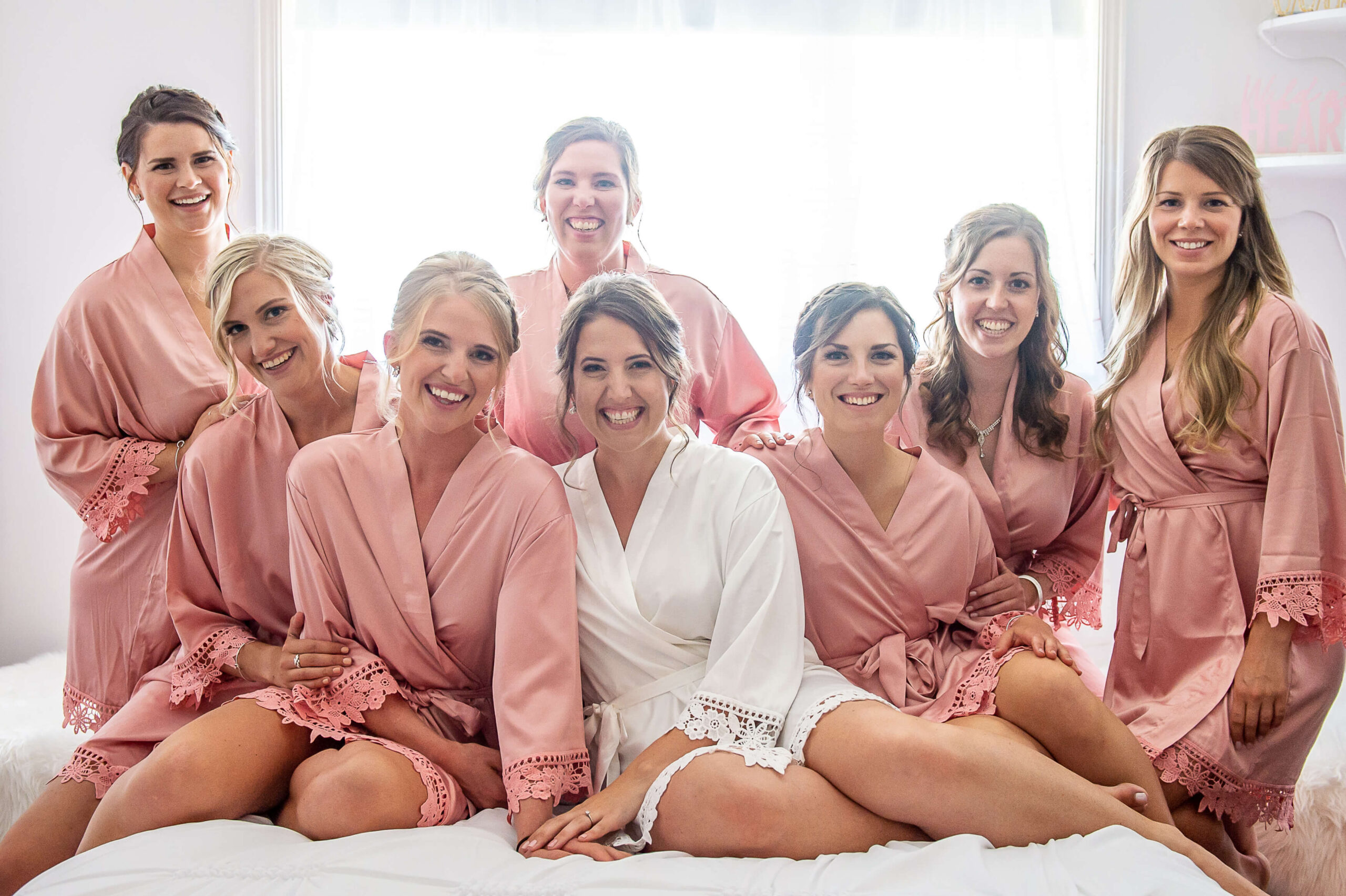 a bride and her bridesmaids sitting on a bed in pretty peach robes