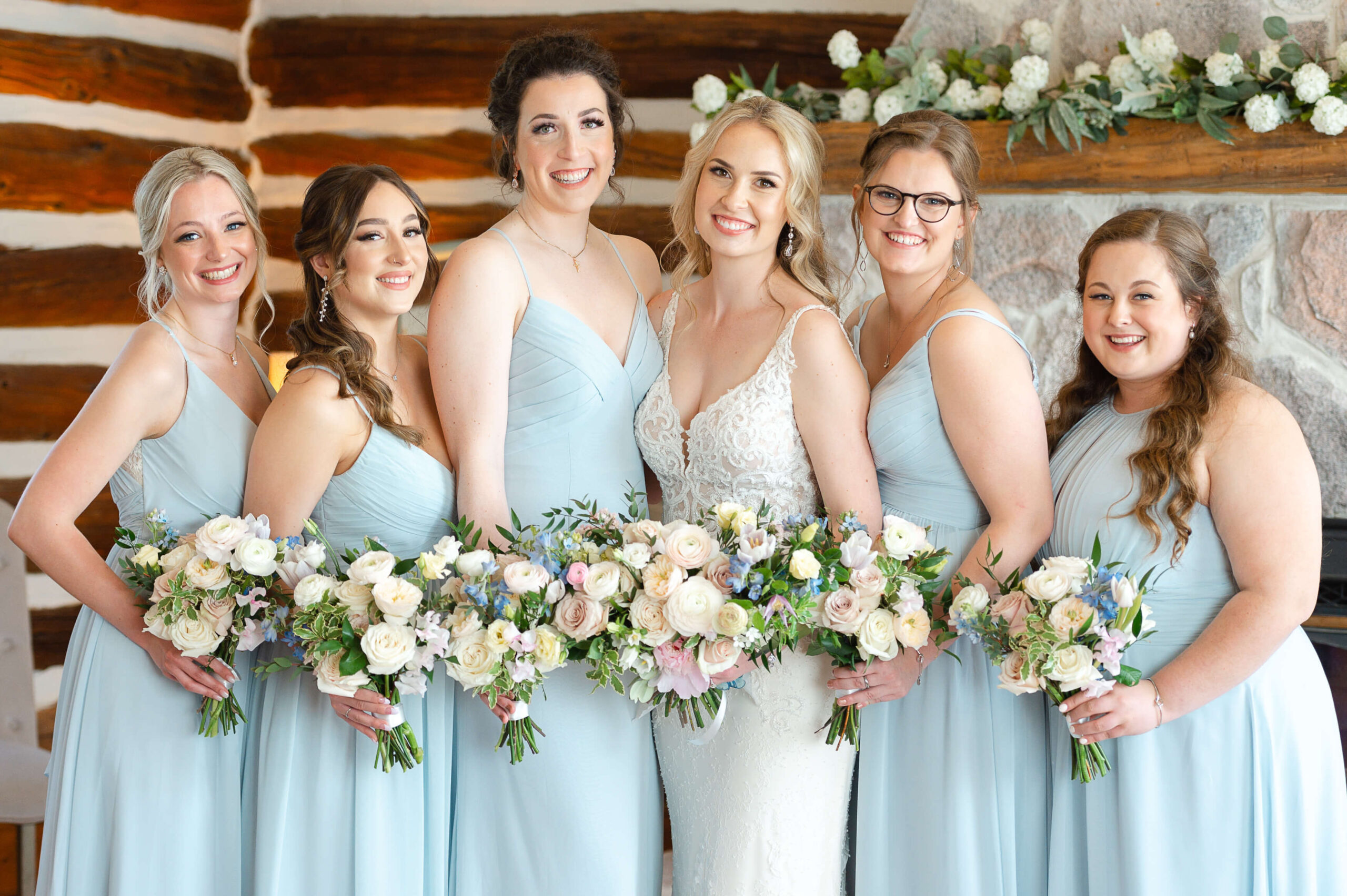 a bride and her bridesmaids in blue Ottawa wedding dresses holding bouquets of pink, blue and yellow flowers