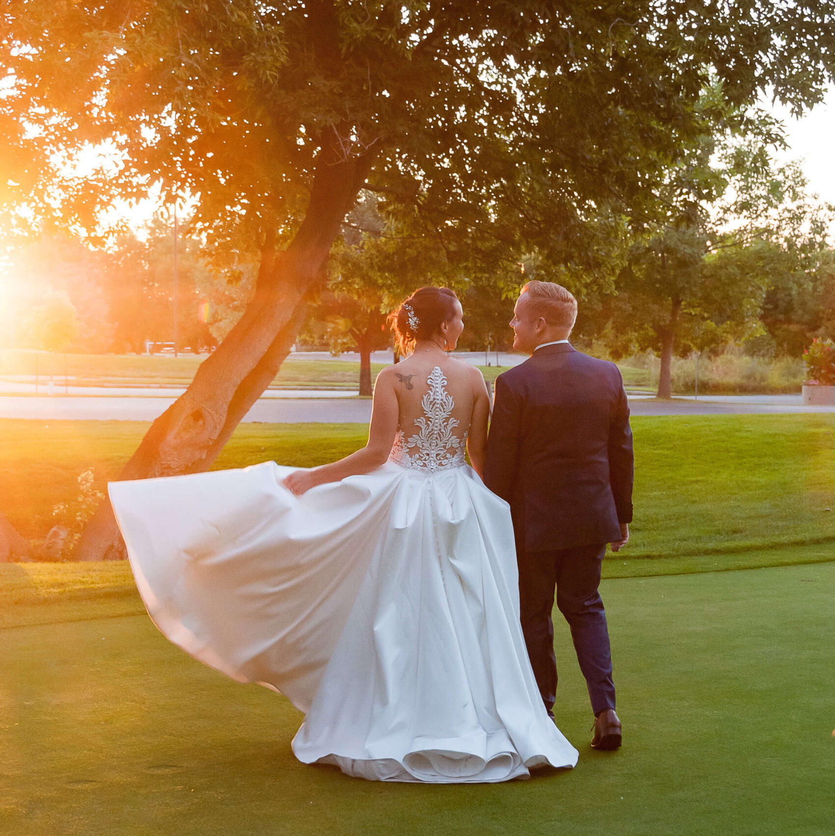 a bride walking and swinging her dress as she walks with her groom in a blue suit on the greens of The Marshes wedding venue