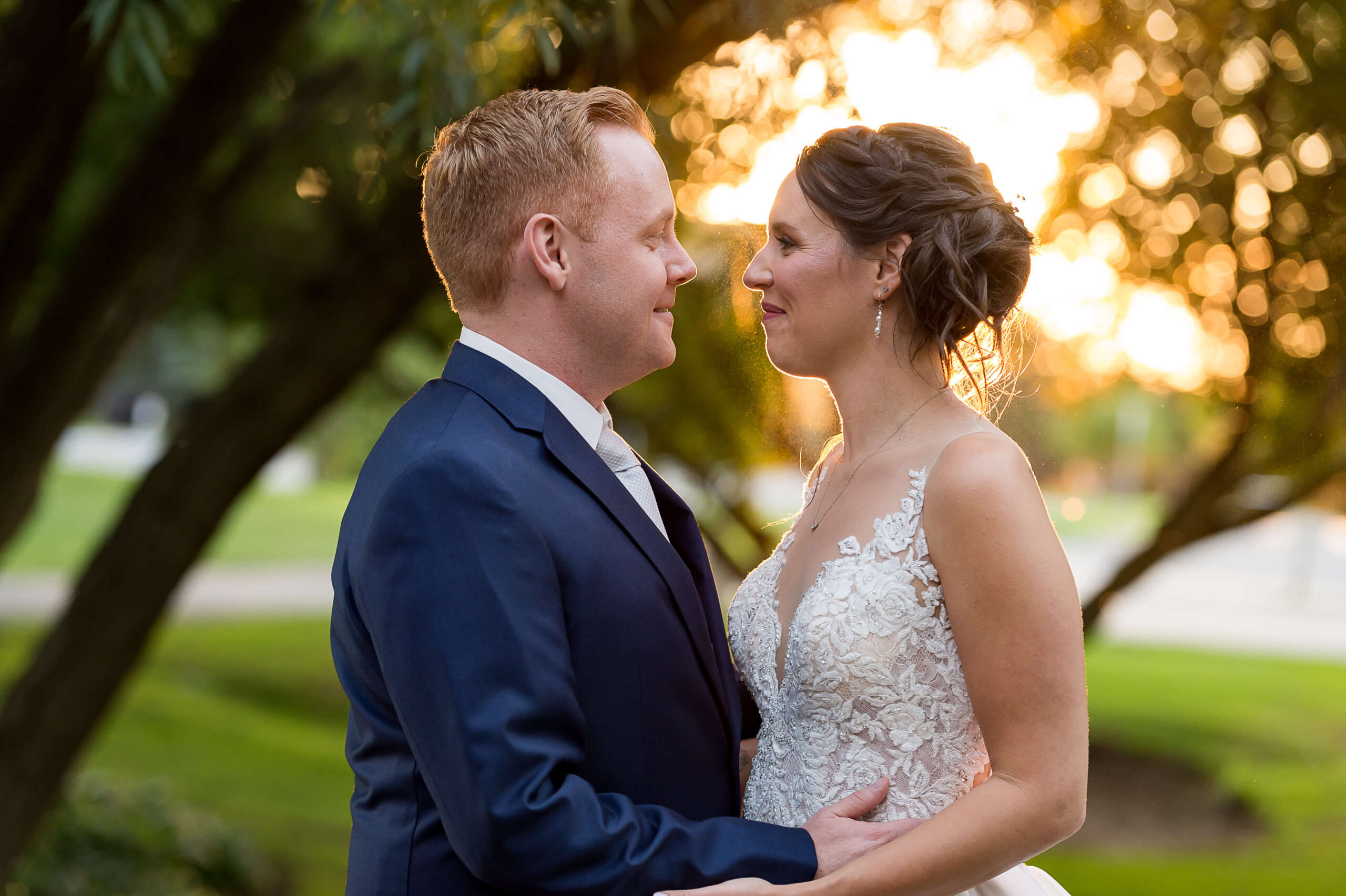 a golden hour sunset photo of a bride smiling into the eyes of her groom in a blue suit. Taken outdoors on the greens of The Marshes wedding venue