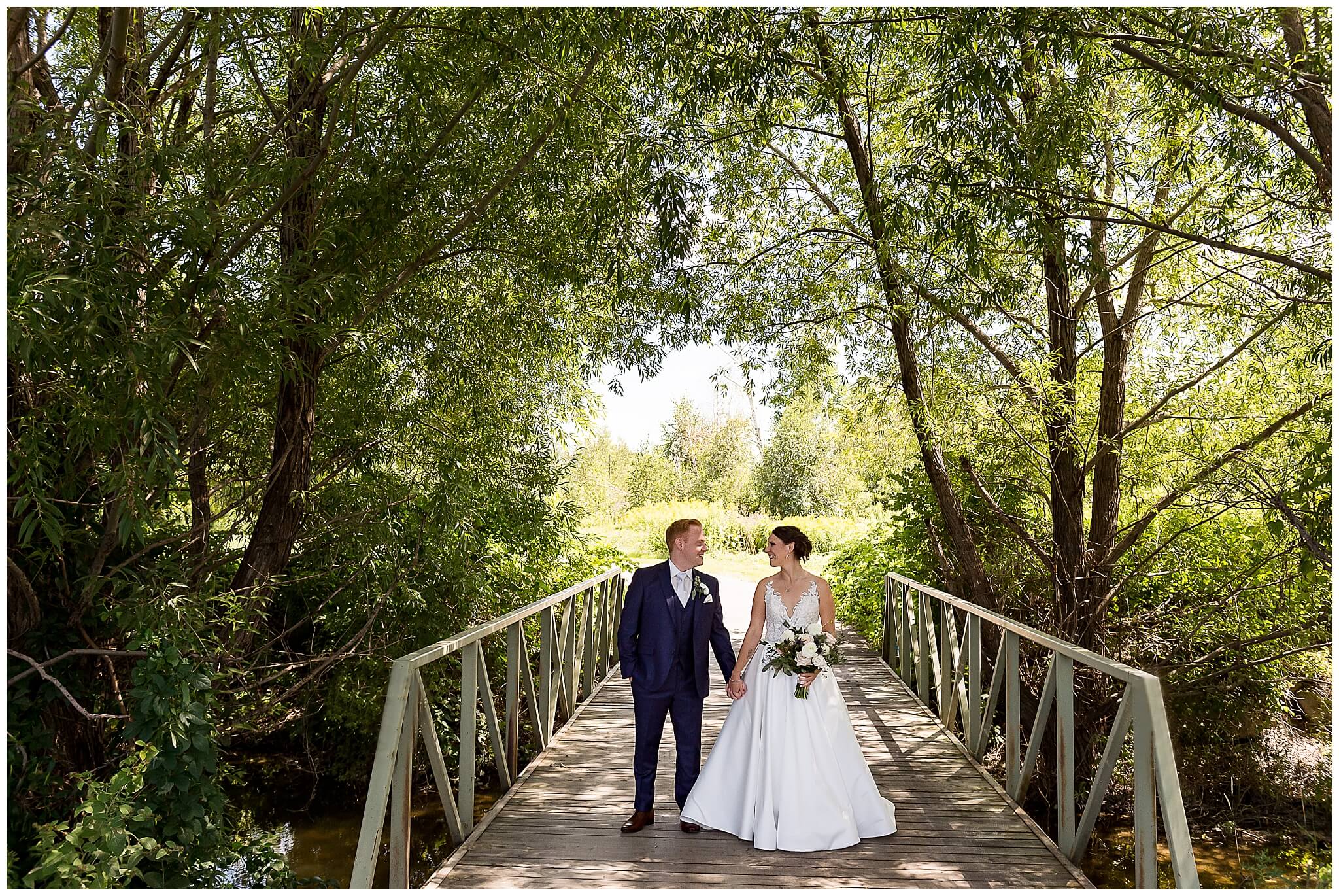 bride in a white dress and a groom in a blue suit holding hands on the bridge of The Marshes wedding venue