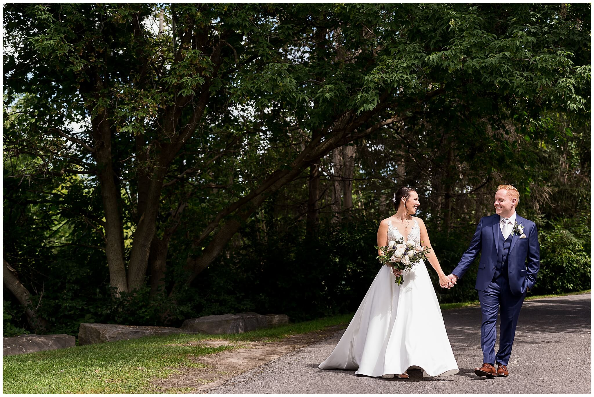 a bride holding a bouquet walks hand in hand with her groom in a blue suit on the grounds of The Marshes wedding venue