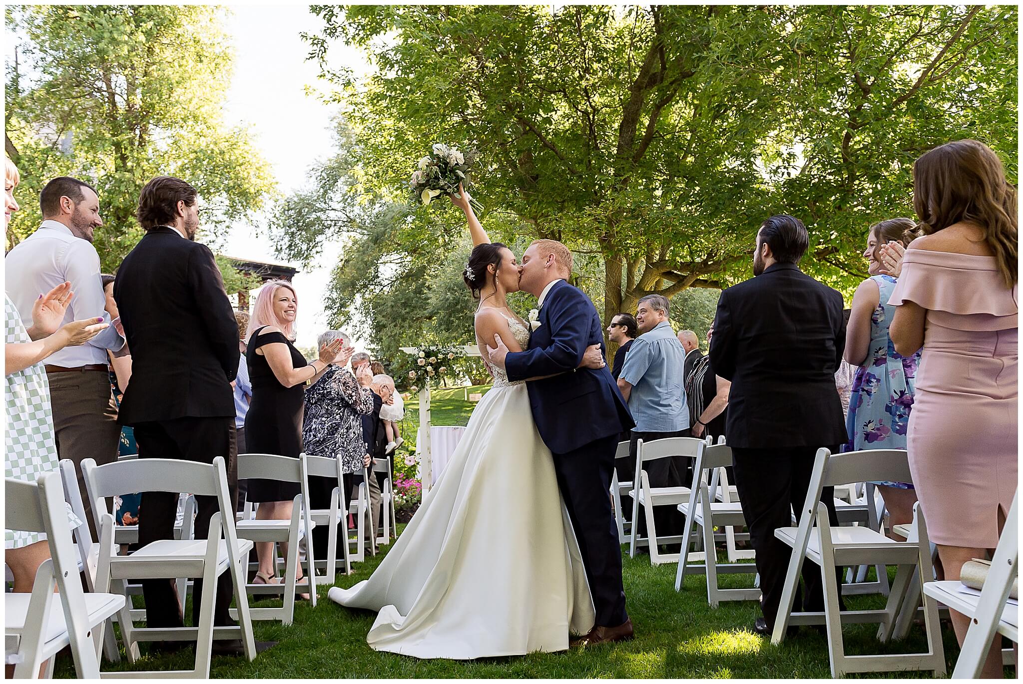 a bride and groom kissing in the middle of the aisle at the end of their ceremony at The Marshes wedding venue