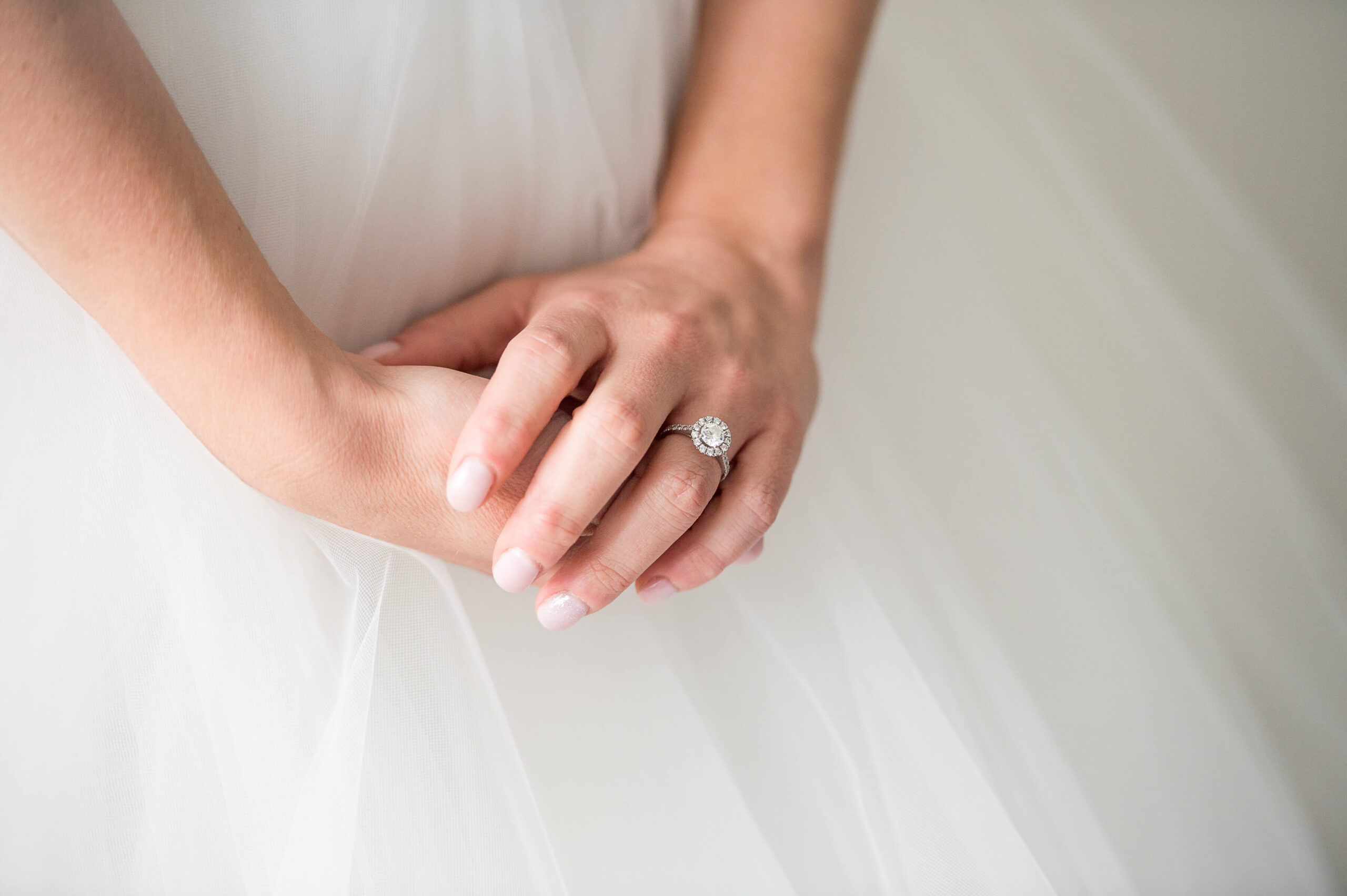 a closeup photo of a bride clasping her hands and holding her engagement ring