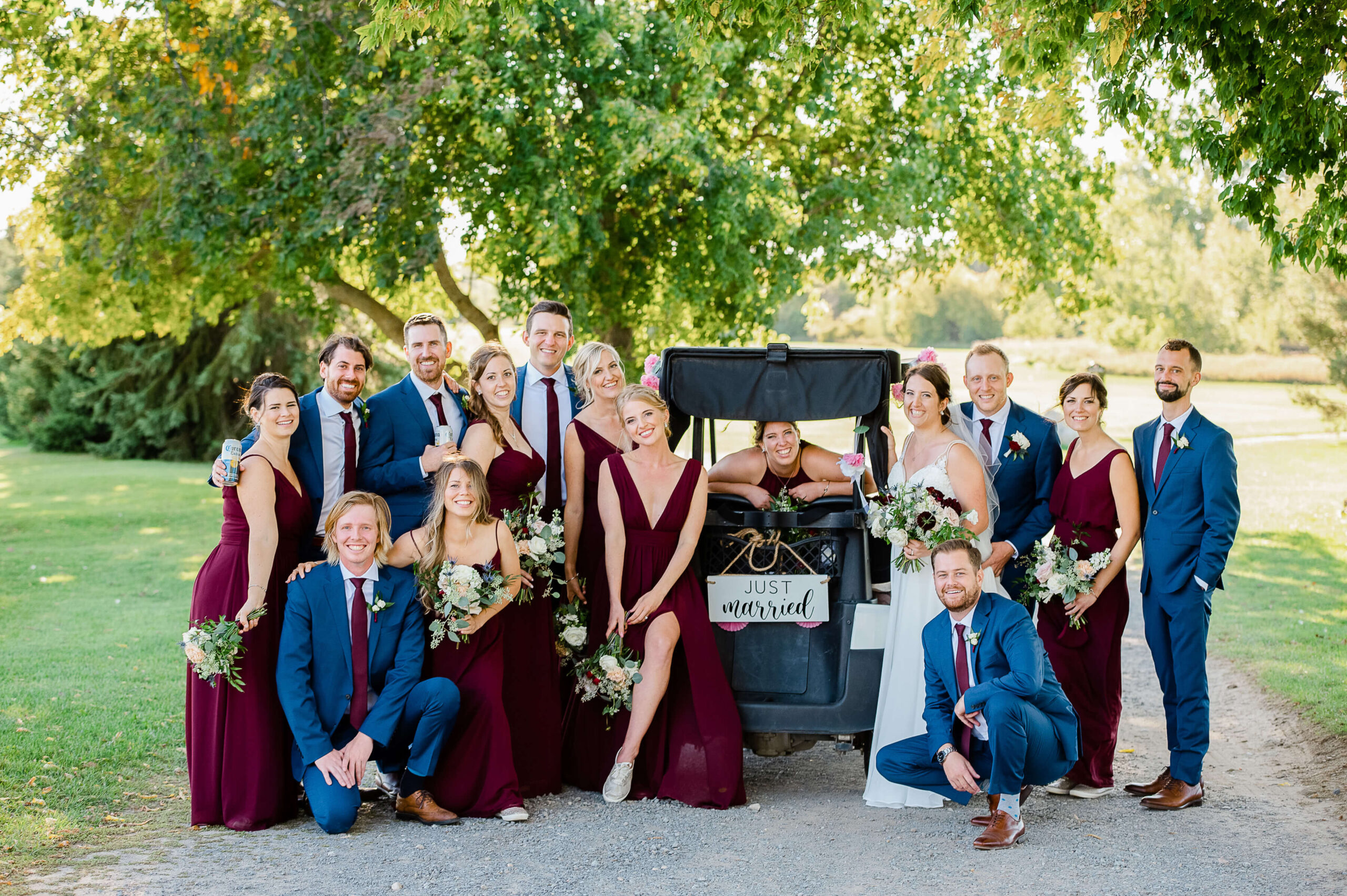 a bride ang groom with their bridesmaids in burgundy and their groomsmen in blue suits around a golf cart. Wedding organized by Opportunity Knocks Events