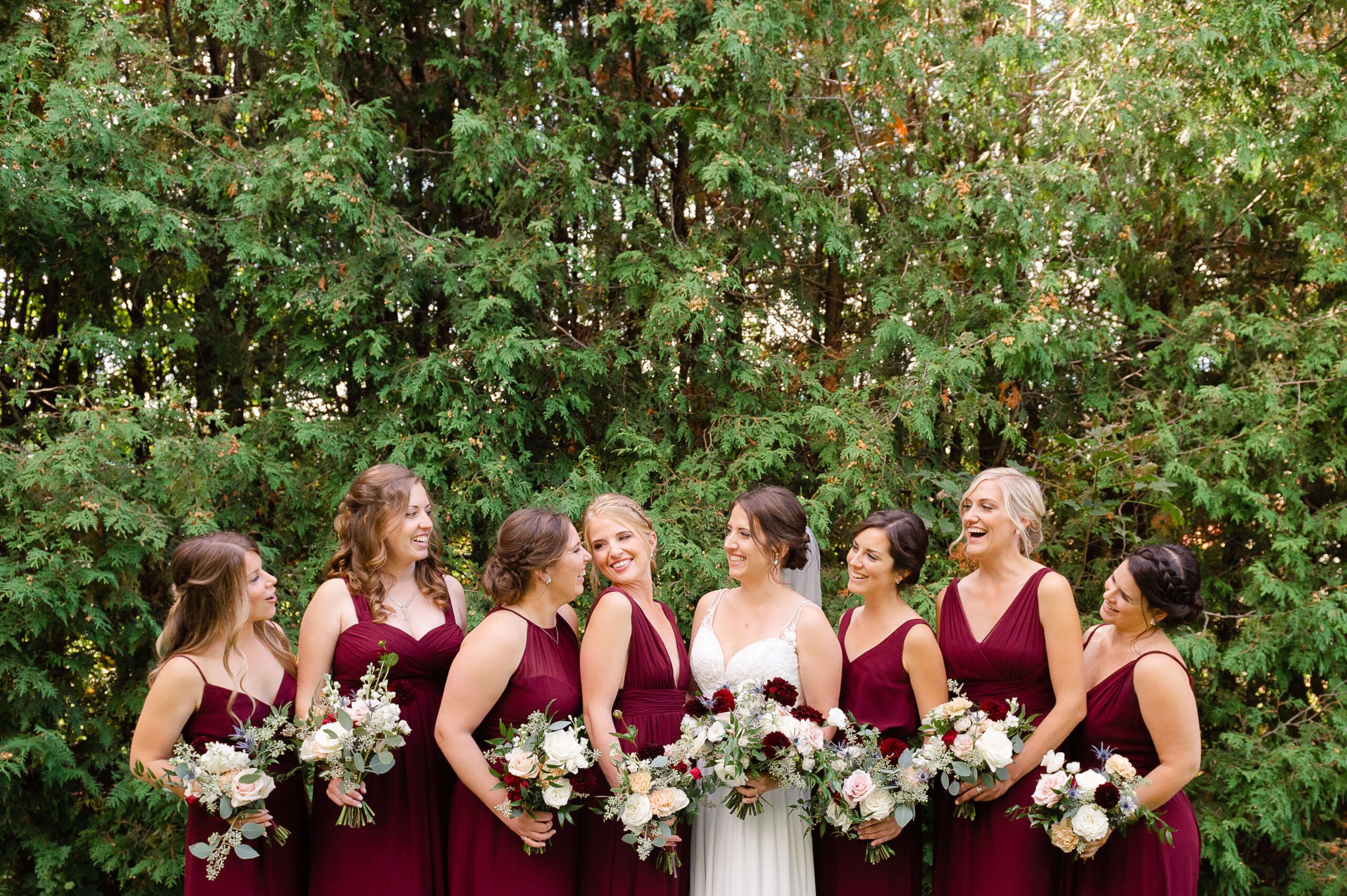 a bride with her bridesmaids dressed in burgundy gowns laughing and giggling just prior to her Opportunity Knocks Events wedding