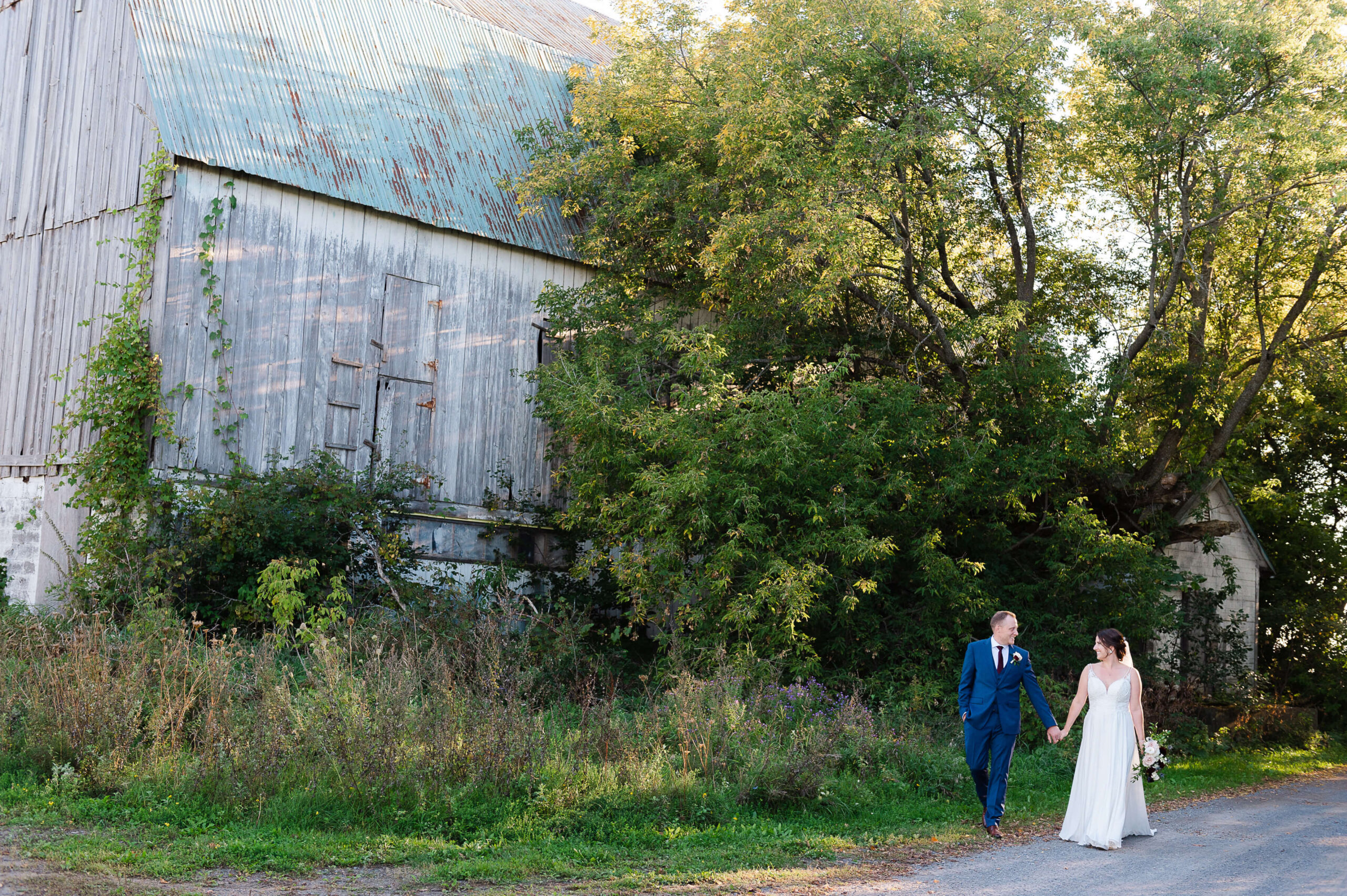a bride and groom walk hand in hand by the barn wedding venue organized by Opportunity Knocks Events