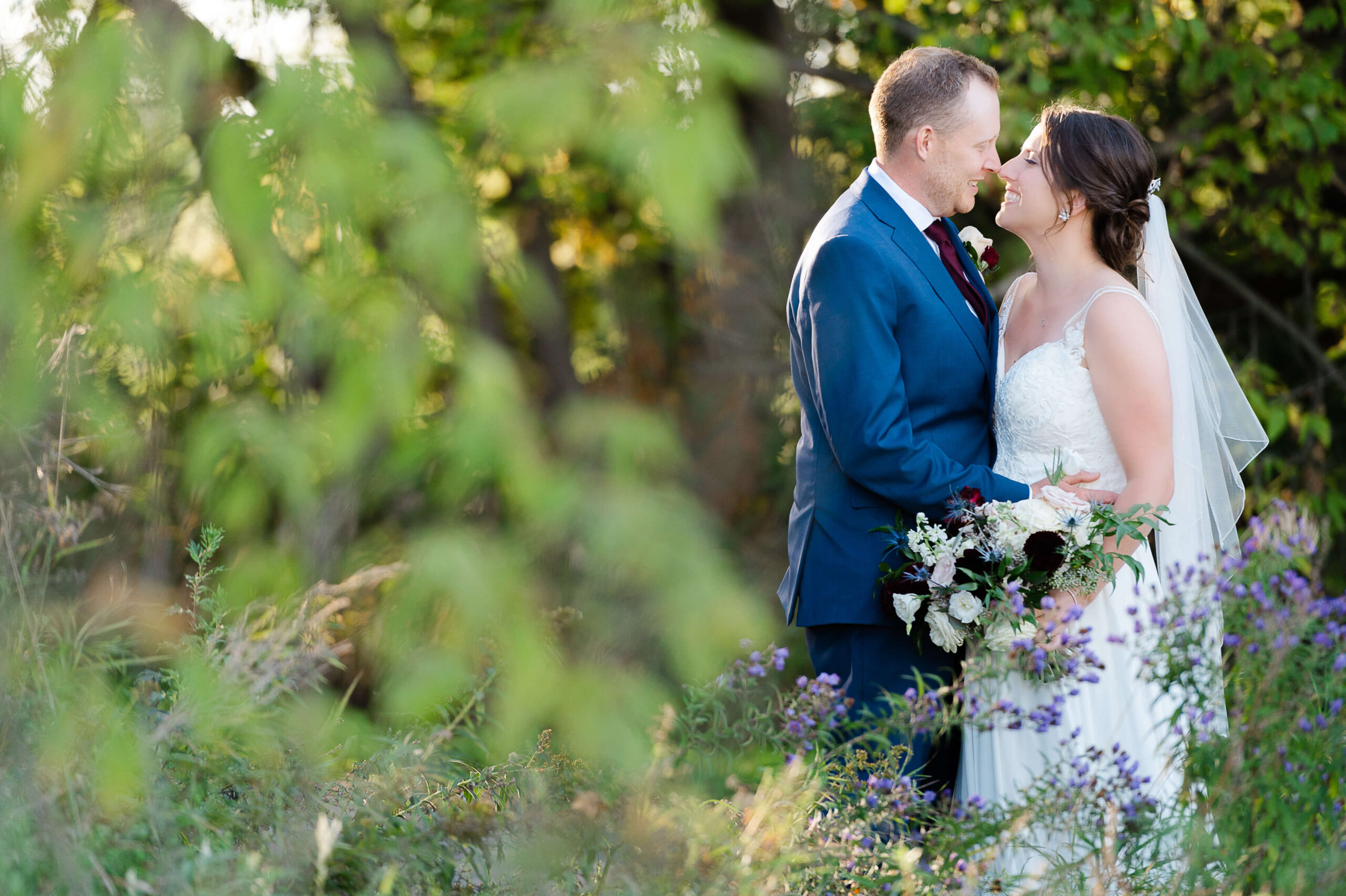 a bride in a white dress and a groom in a blue suit nuzzle noses during a wedding organized by Opportunity Knocks Events