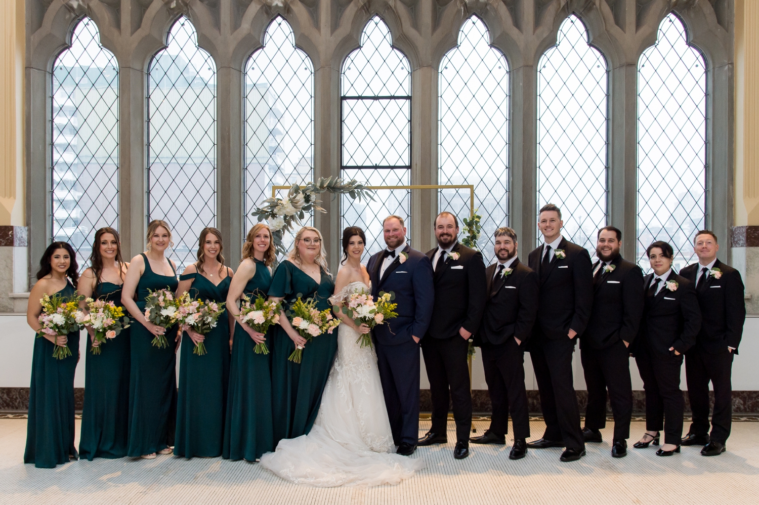 a formal portrait of a wedding party with the bridesmaids in green dresses and the groomsmen in tuxedos. 