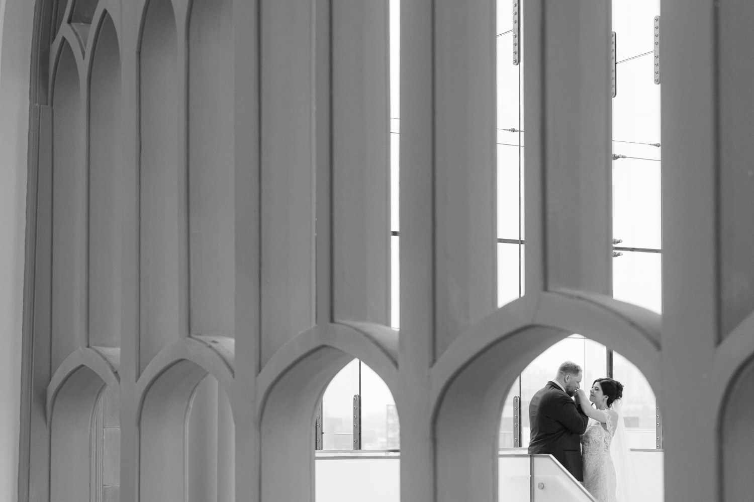 a black and white shoot through photo of a groom kissing his bride's hand in the Queen's Lantern as part of their Museum of Nature Wedding Photos
