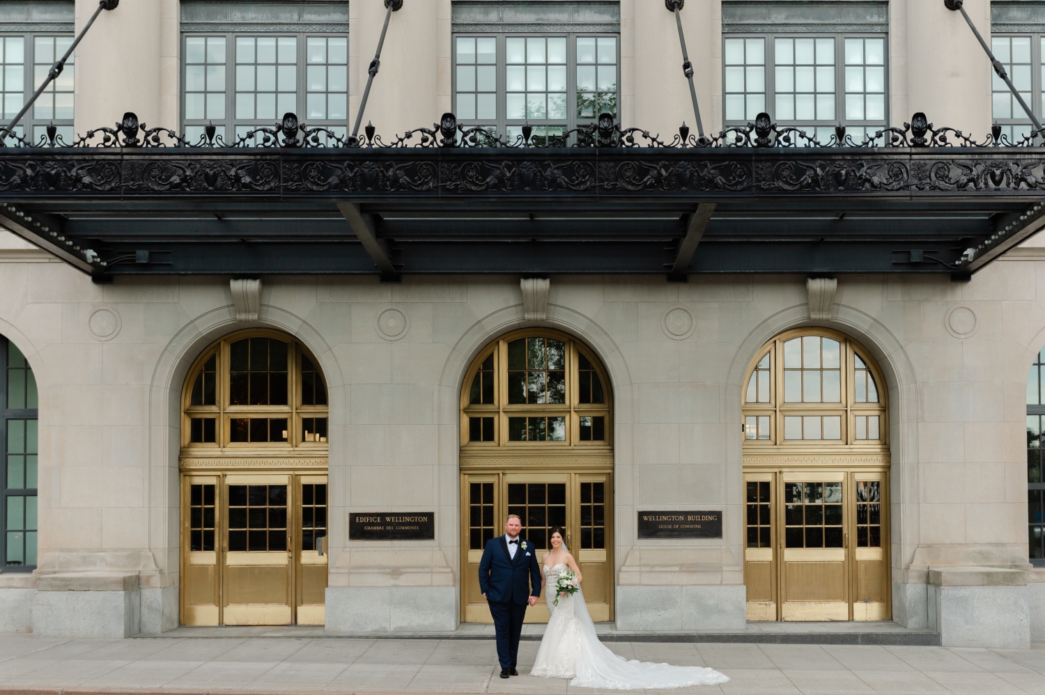a bride and groom holding hands and standing in front of the Wellington Building in Ottawa as part of their Museum of Nature Wedding Photos
