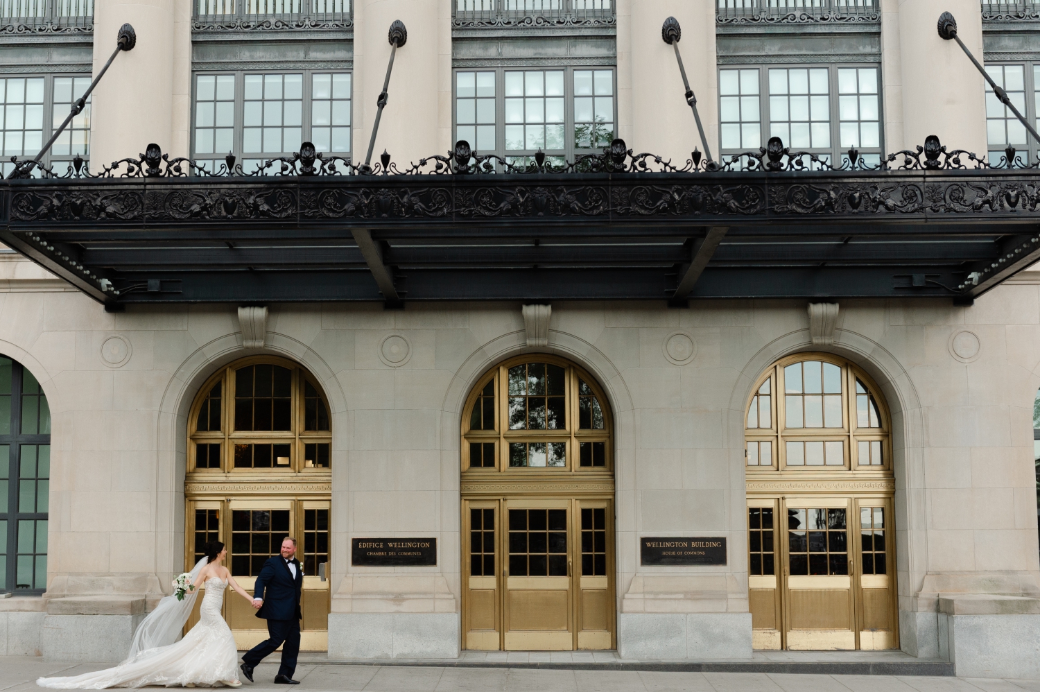 a bride and groom holding hands and running in front of the Wellington Building in Ottawa as part of their Museum of Nature Wedding Photos