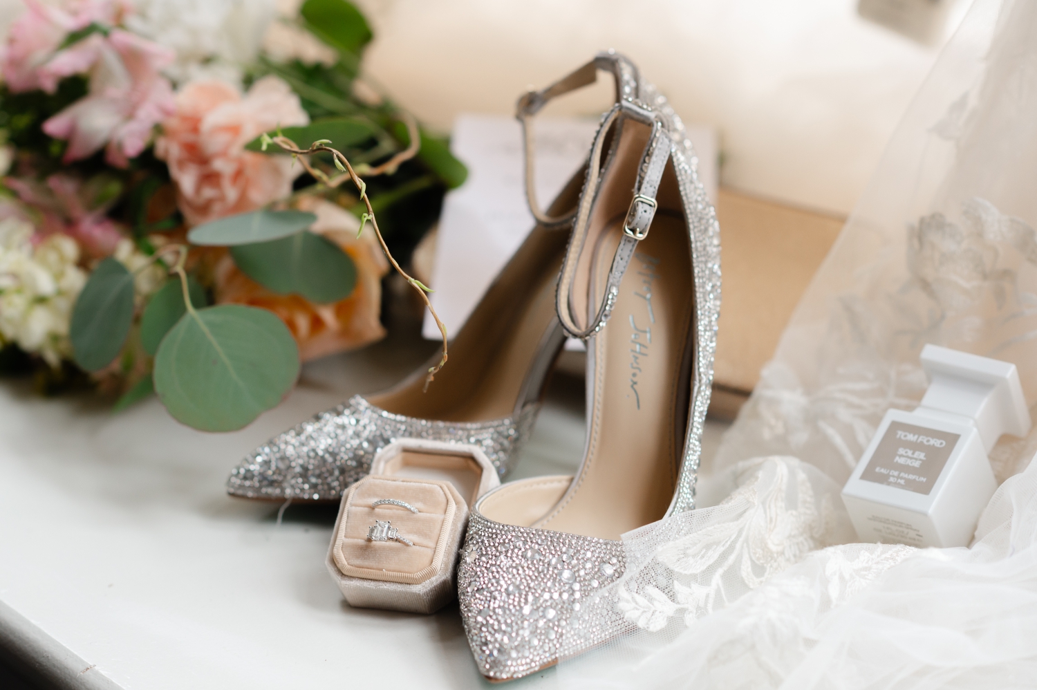 a closeup photo showing a brides sparkly shoes, wedding ring set, perfume and bouquet. Captured in the Restays hotel oy Ottawa wedding photographer JEMMAN Photography