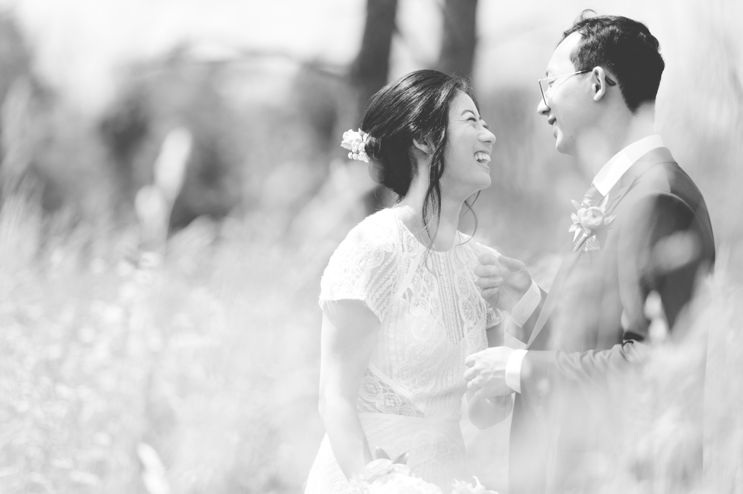 a black and white photo of a bride and groom laughing with the foreground blurred. Captured by Ottawa wedding photographer JEMMAN Photography