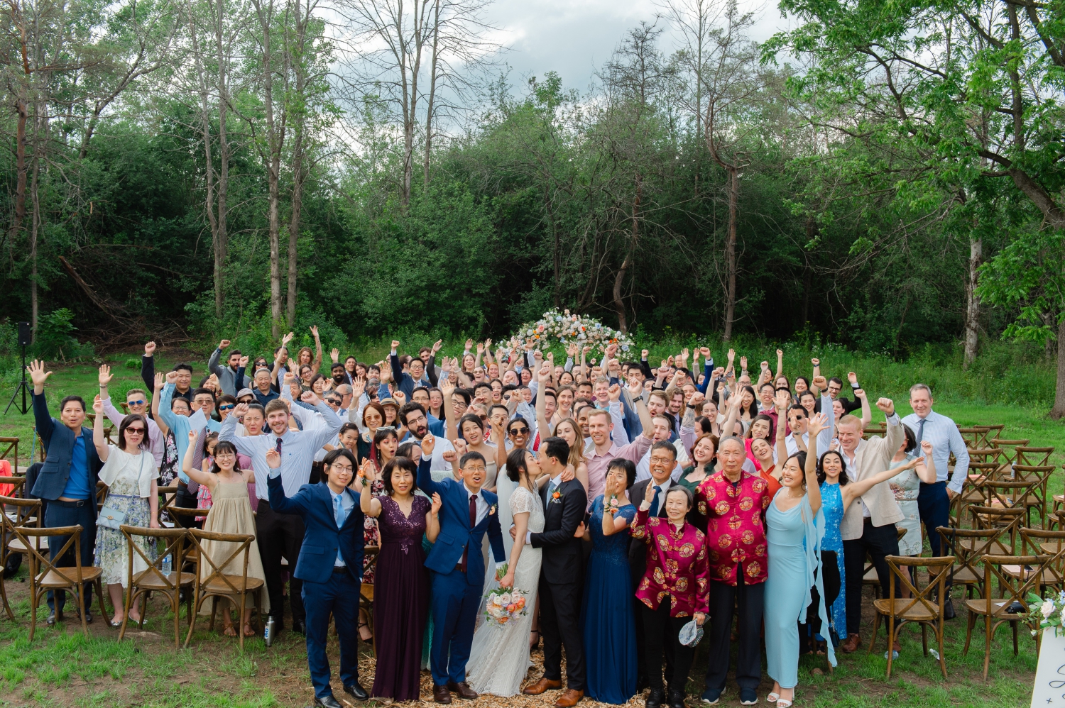 a group photo of a bride and groom and all their guests cheering taken at the end of their Ottawa backyard wedding ceremony