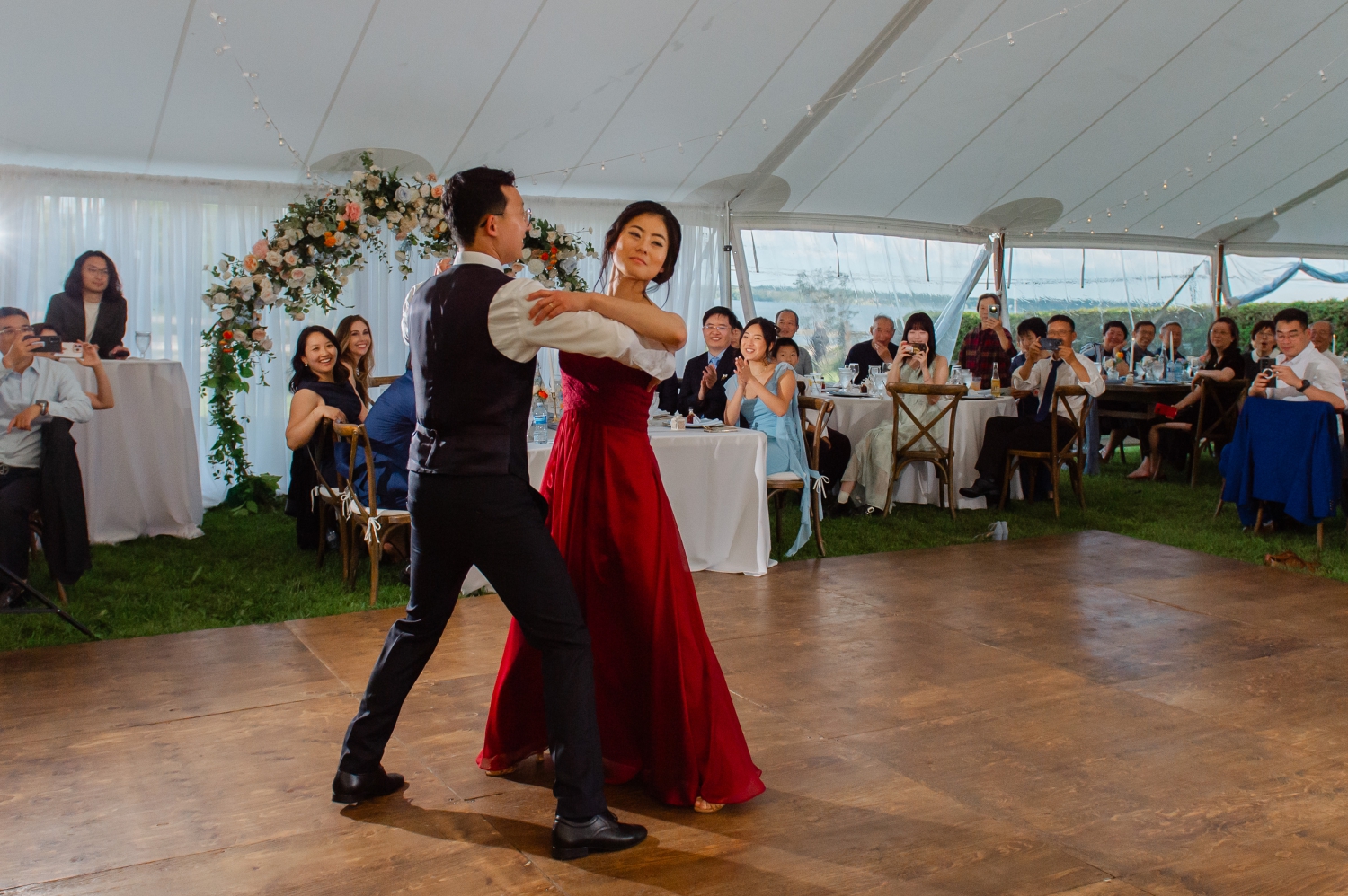a bride in a red dress and a groom in black suit in an elegant dance pose as part of their choreographed first dance during their Ottawa backyard wedding reception