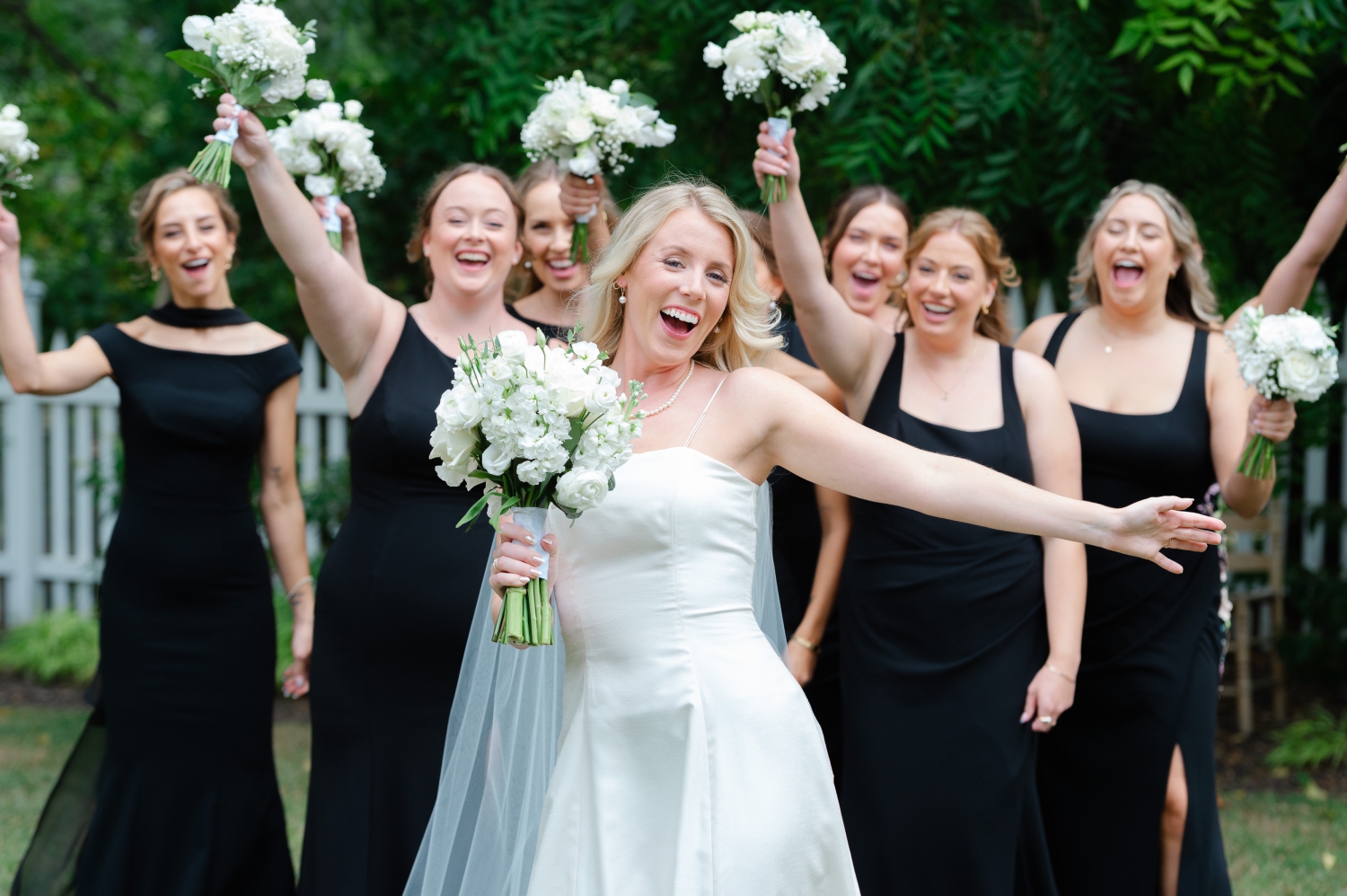 a bride laughing and being playful in front of her bridesmaids dressed in black gowns as they leave for the bride's Ottawa tented wedding ceremony