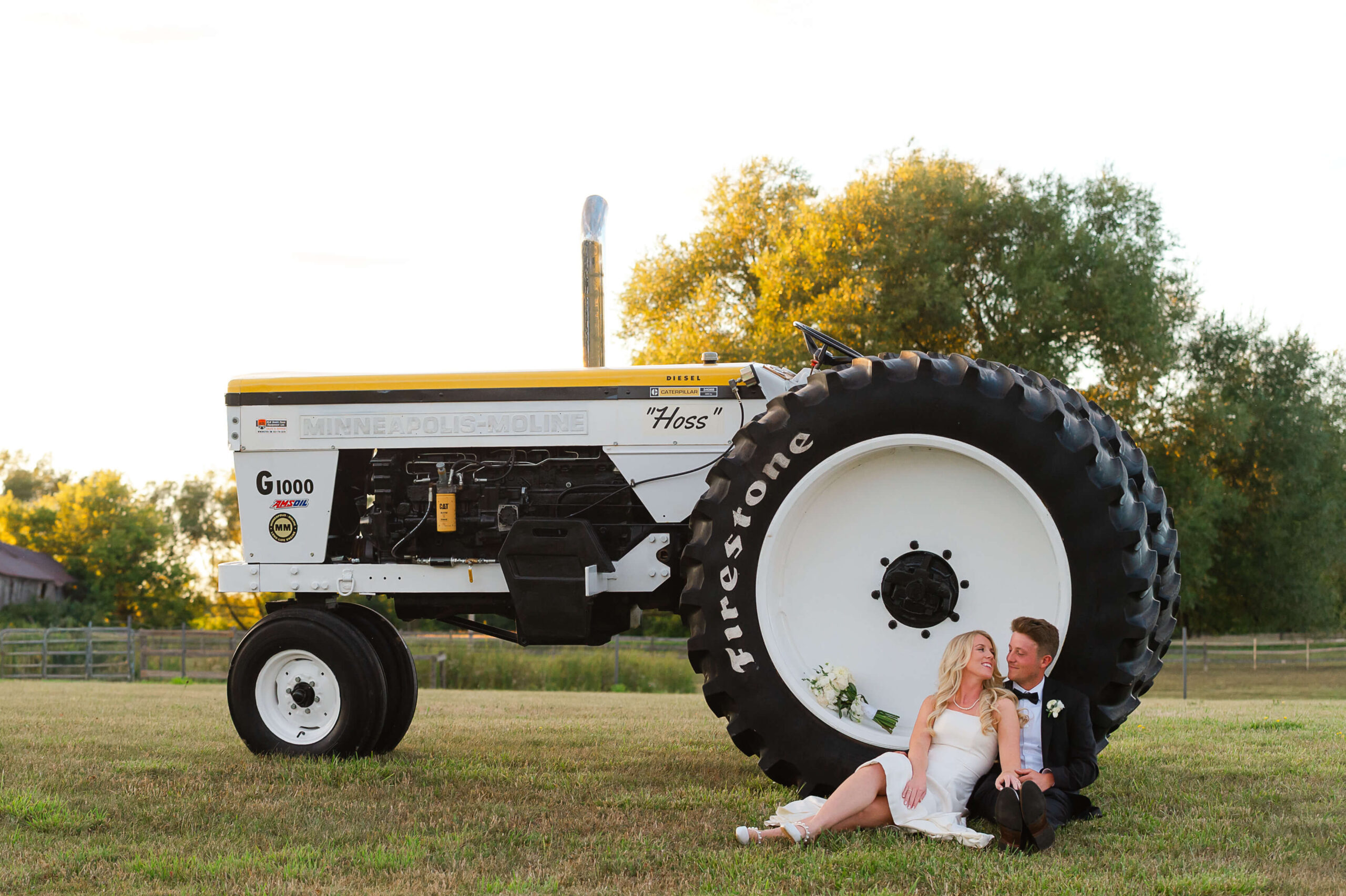 a bride and groom sit in the wheel of a farming tractor as part of their Ottawa tented wedding photography