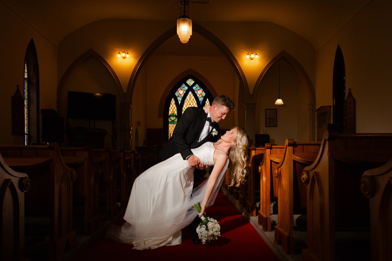 a bride and groom do dip at the end of their ceremony aisle. Captured indoors by Ottawa wedding photographer JEMMAN Photography