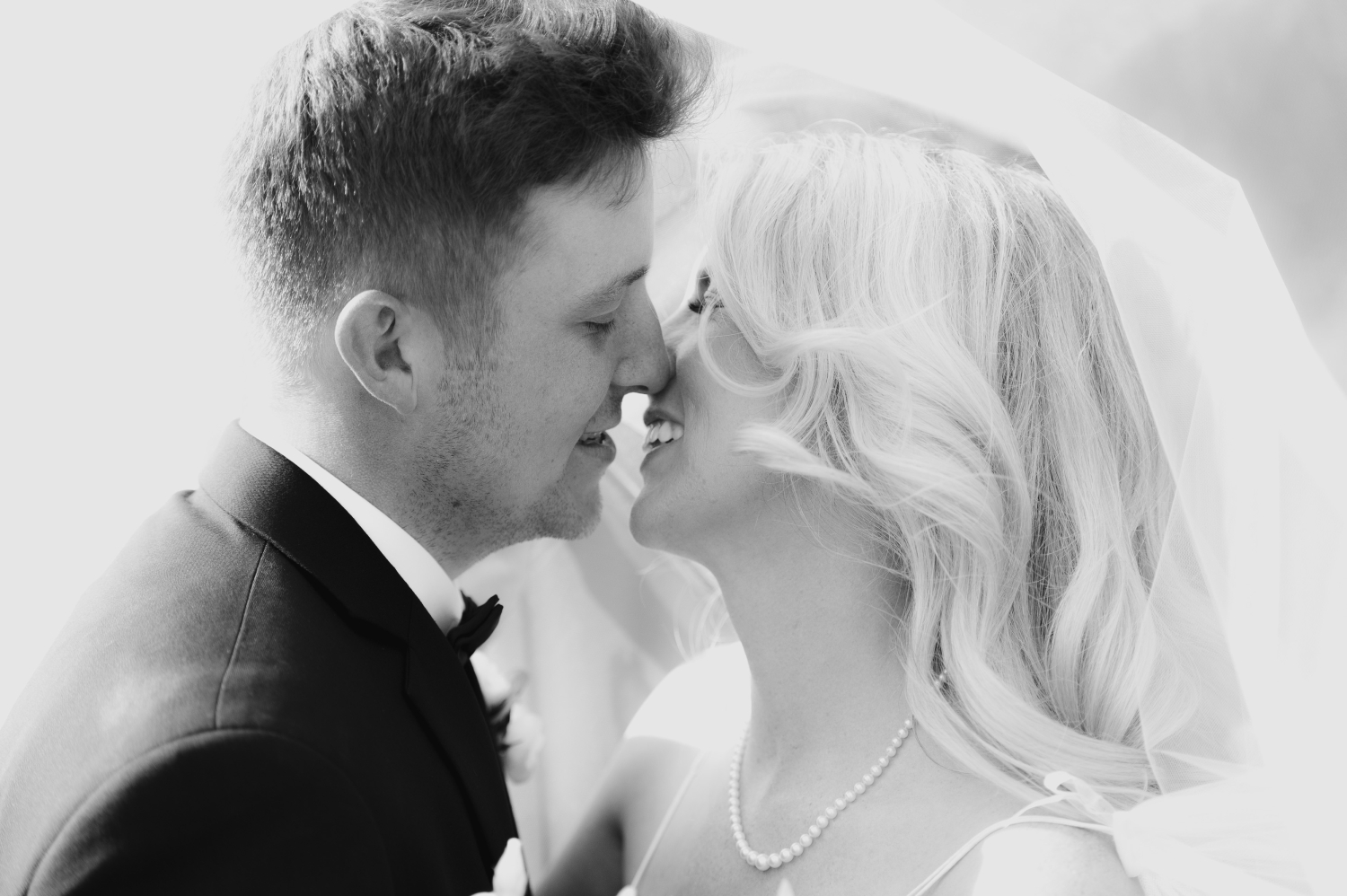 a black and white photo of a bride and groom kissing under a veil. Captured by Ottawa wedding photographer JEMMAN Photography