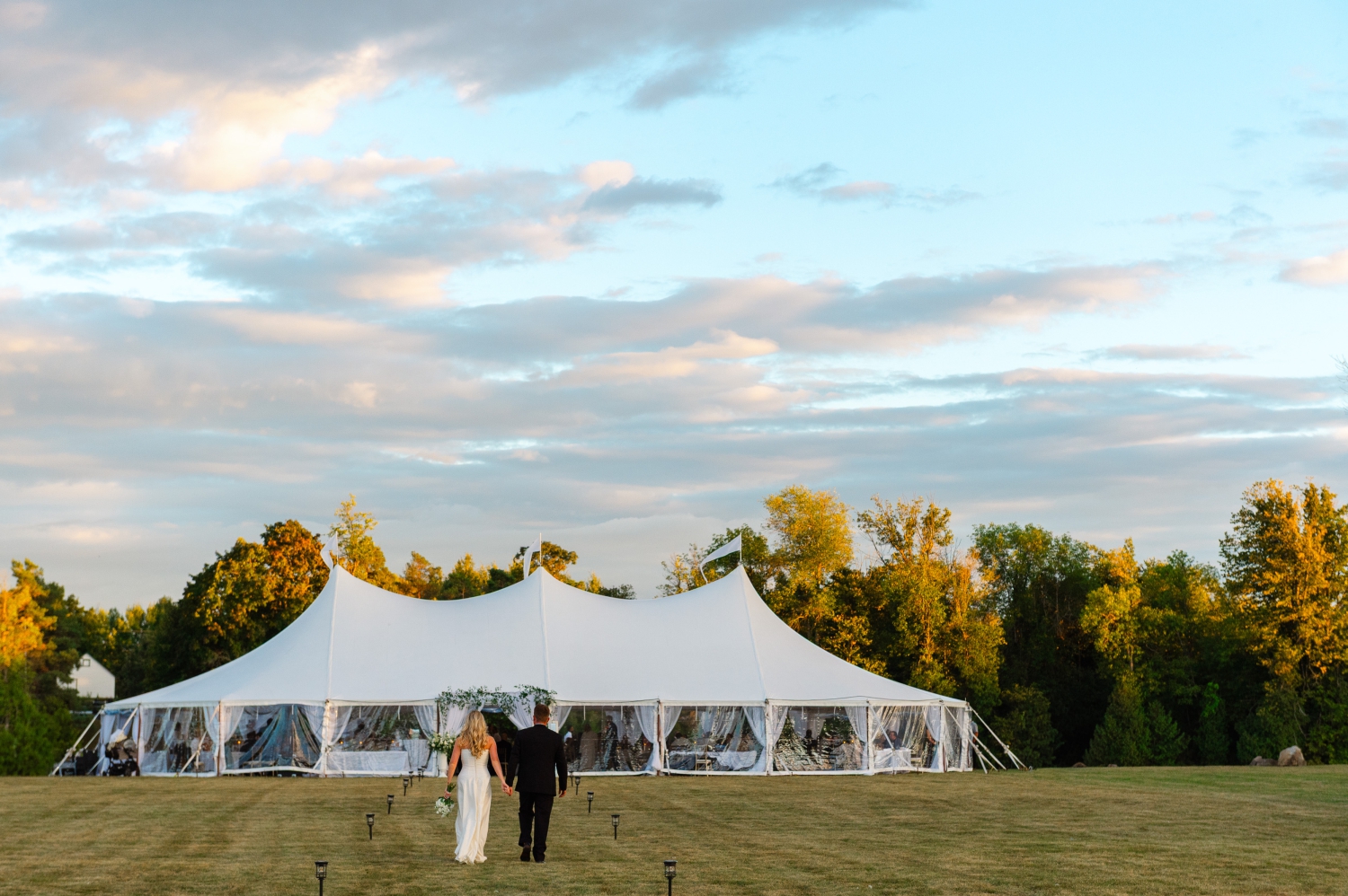 a bride and groom walking hand and hand towards their Ottawa tented wedding reception