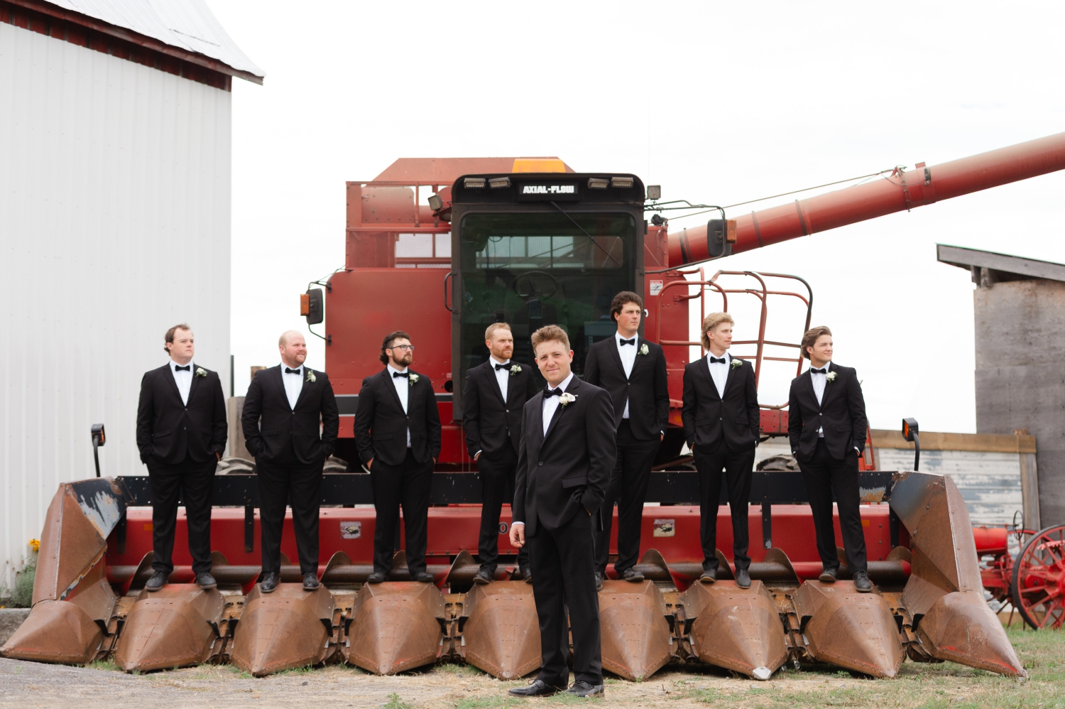 a dramatic photo of a groom standing in front of a combine with his seven groomsmen standing on it. Captured as part of the groom's getting ready photos for his Ottawa tented wedding
