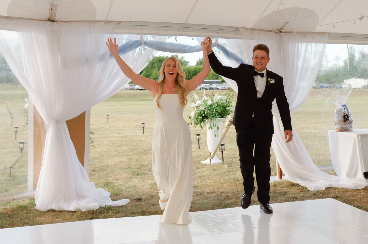 a bride and groom entering their Ottawa tented wedding reception smiling and waving their arms in the air as they're announced