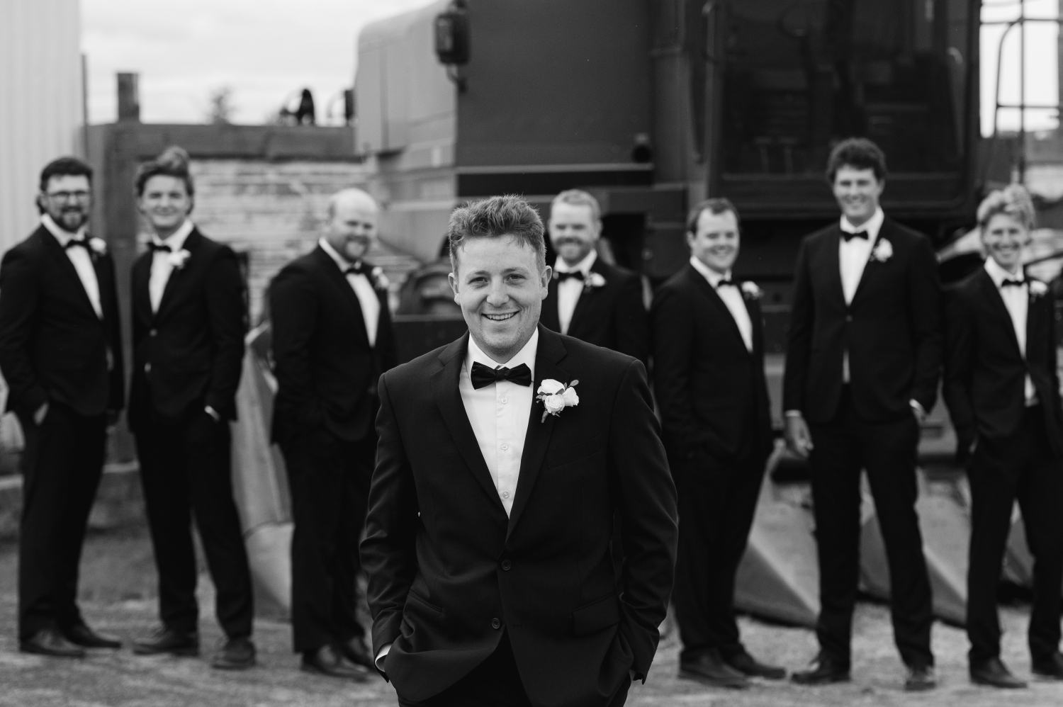 a black and white photo of groom in a tuxedo walking and his groomsmen behind him smiling. Captured by JEMMAN Photography as the groom gets ready for his Ottawa tented wedding