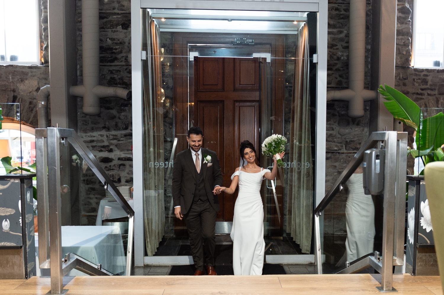 a bride and groom entering their reception through the main doors of Restaurant 18 and waving their arm and bouquet in the air