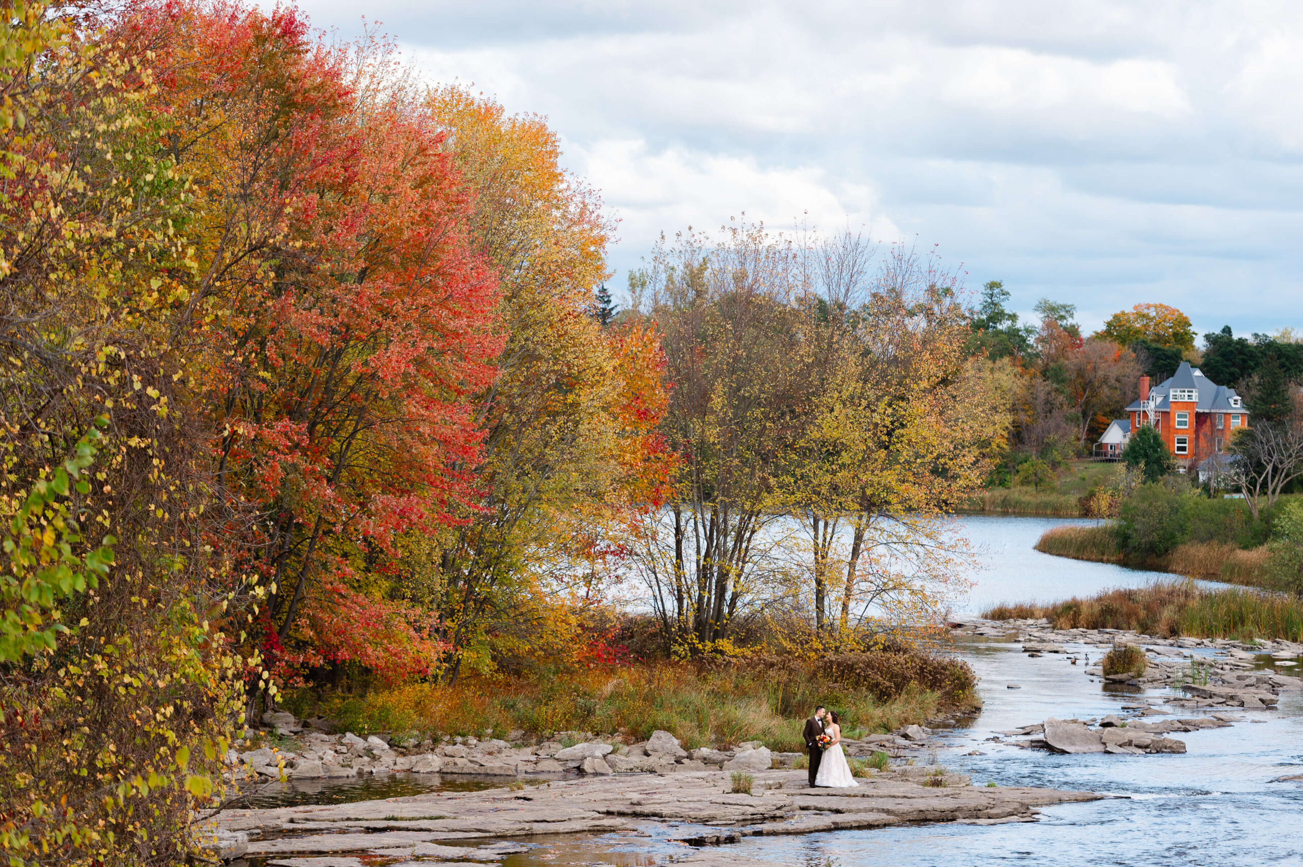 a bride and groom surrounded by fall foliage and kissing on the rocks of the Merrickville Ruins as part of the Maple and Rose wedding photos