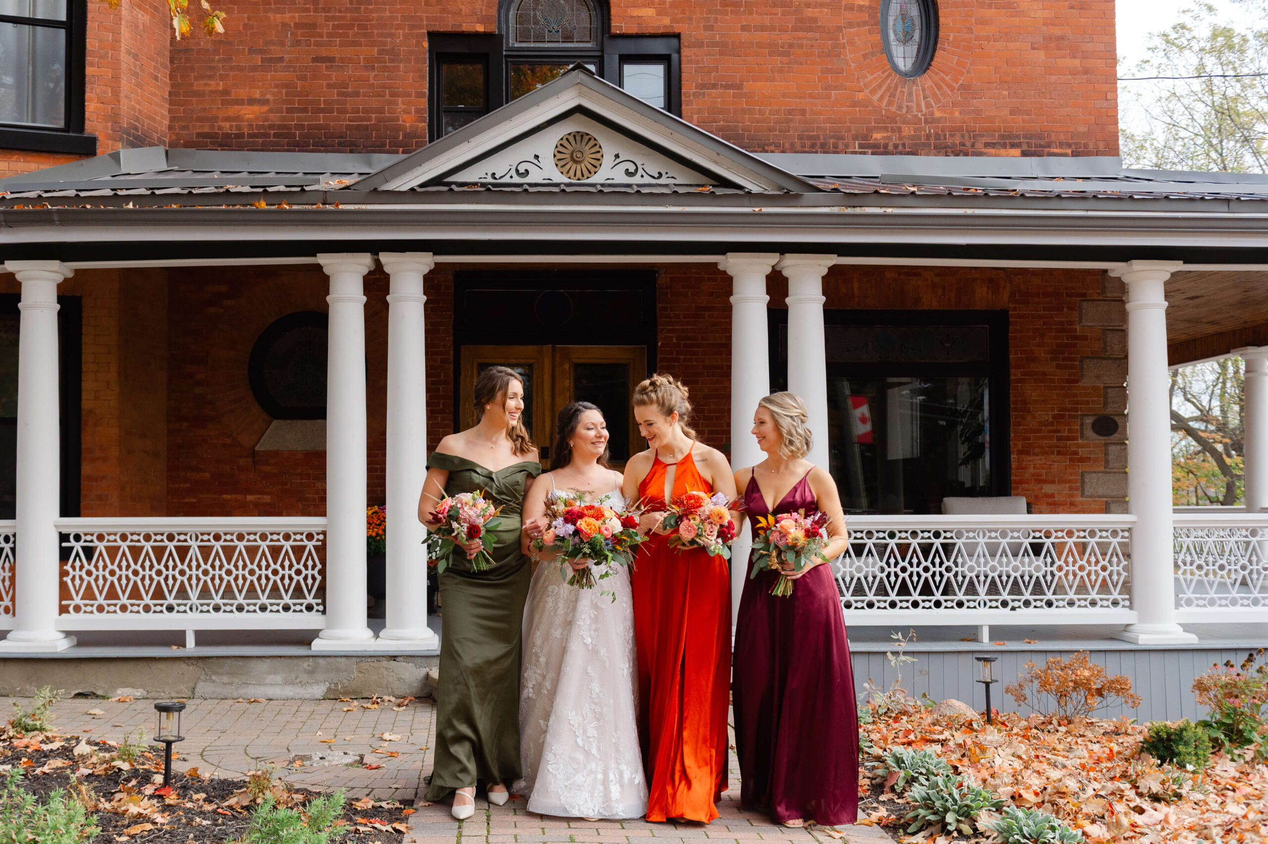 a bride and her bridesmaids in fall coloured dresses walking outside of the Maple and Rose wedding venue. Captured by JEMMAN Photography