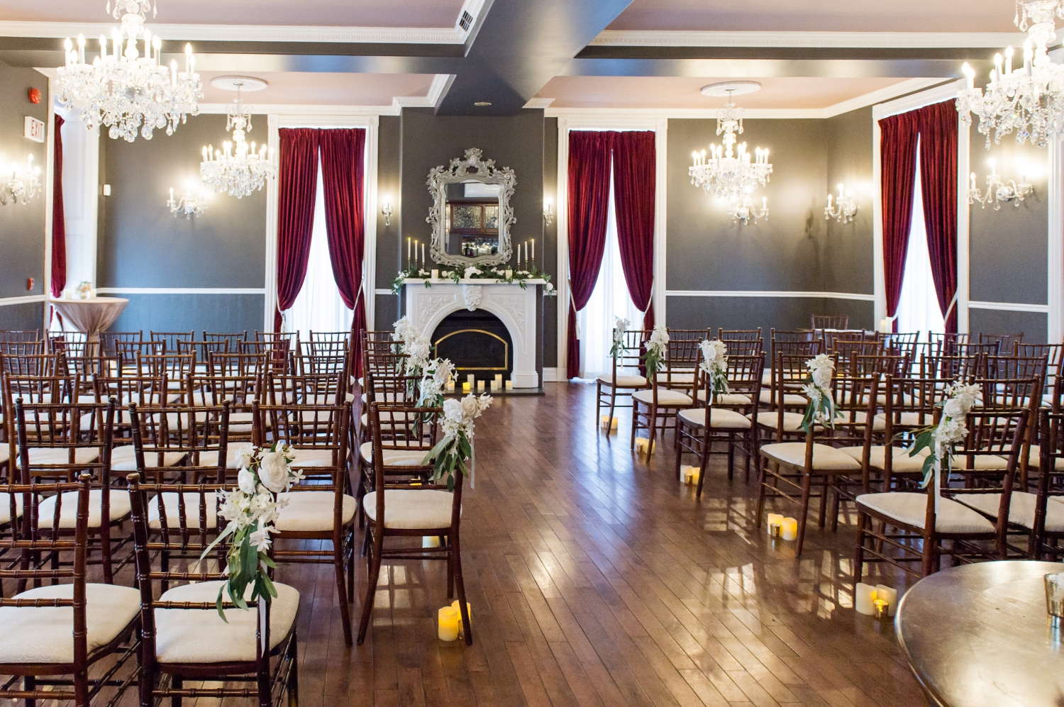 the ceremony setup of the Grand Hotel Weddings showing chivari chairs, fireplace, velvet curtains, grey walls and chandeliers. Captured by JEMMAN Photography