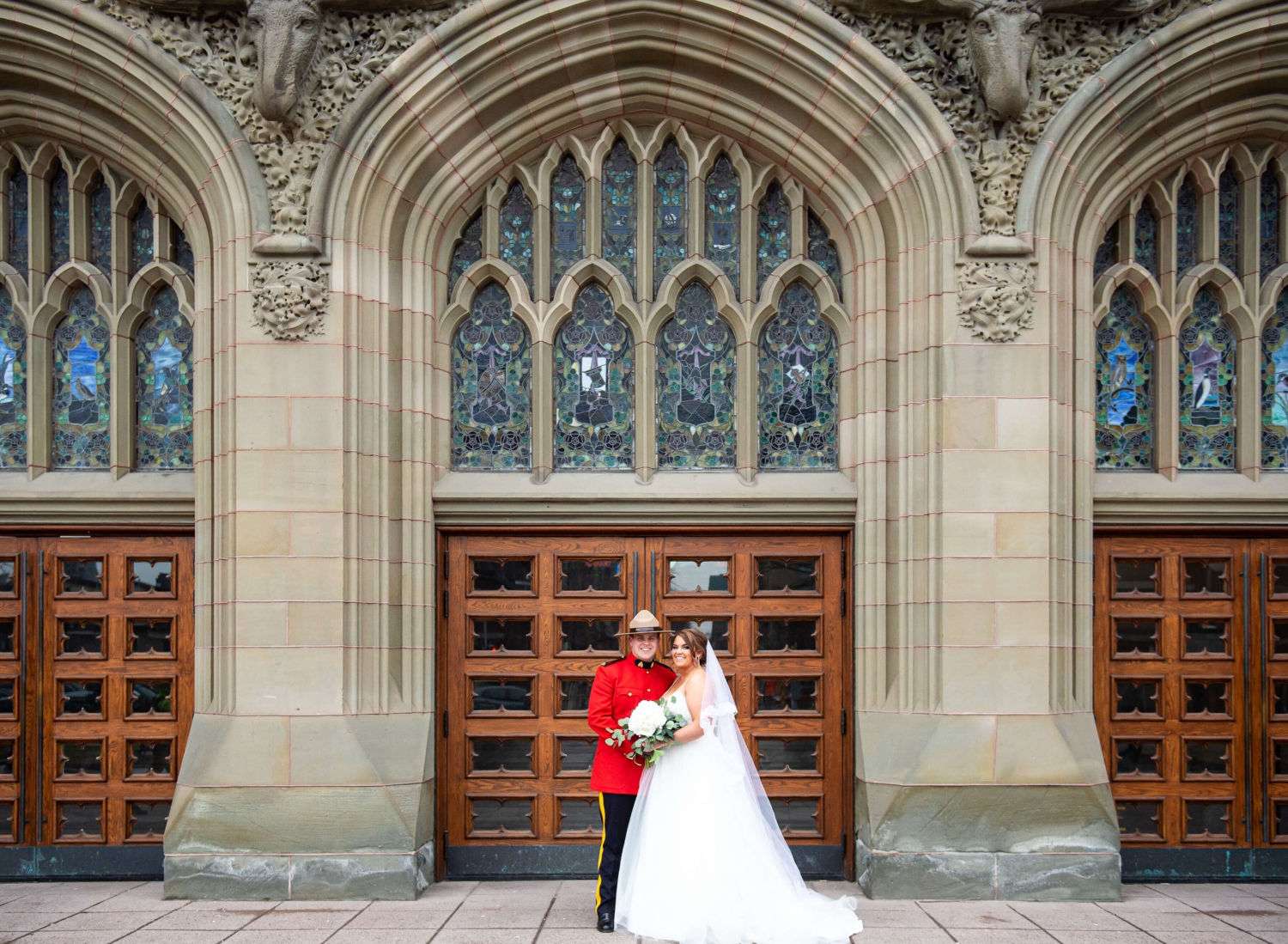 a portrait of a bride in a white ballgown and veil and a groom in the red RCMP serge outside the main doors of the Museum of Nature, one of the downtown Ottawa wedding venues. Captured outdoors by JEMMAN Photography