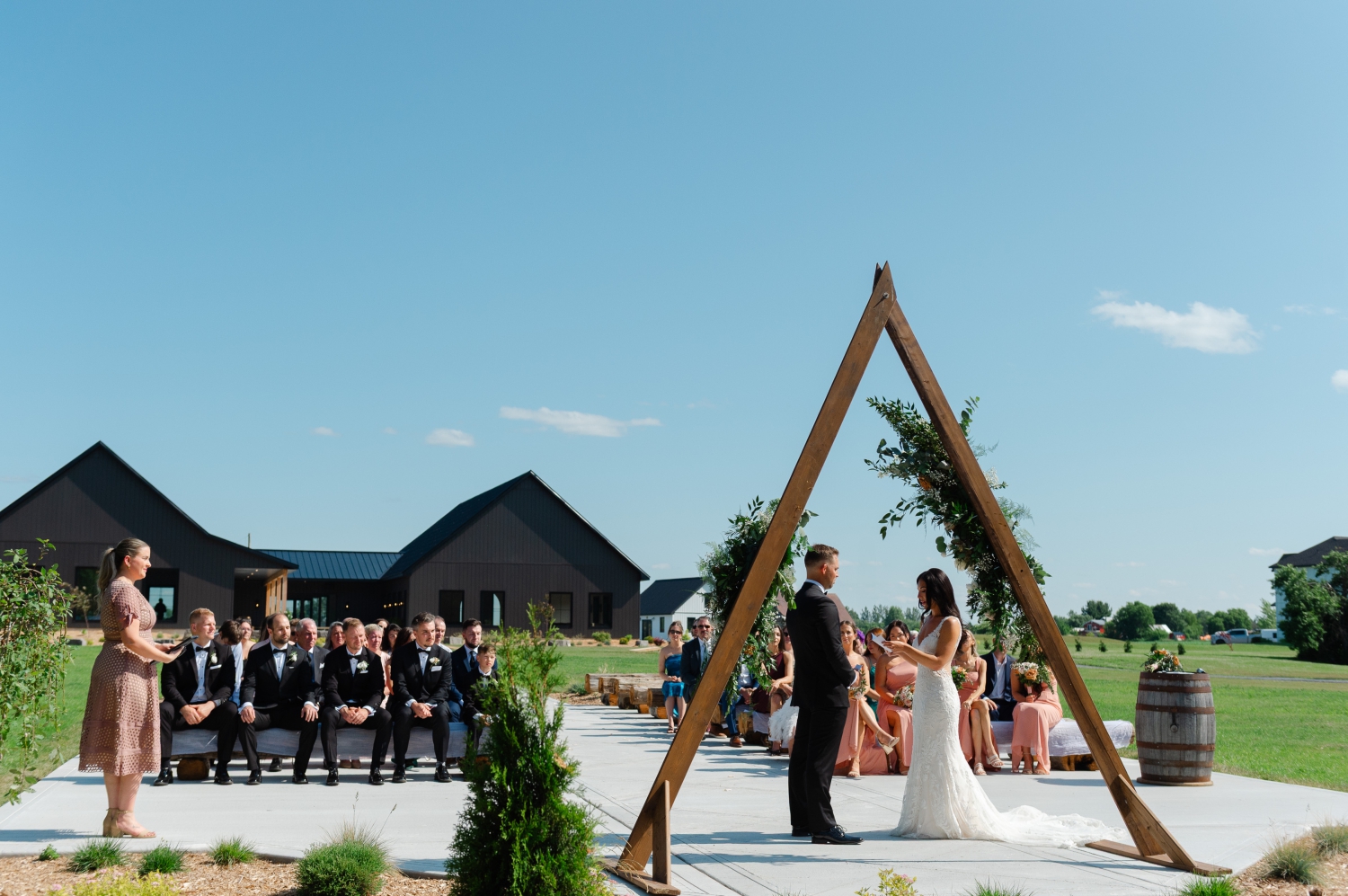 a wide angle photo of a bride and groom exchanging wedding vows while their guests look on. Captured at the Ottawa outdoor wedding venue, Bleeks and Bergamot by JEMMAN Photography
