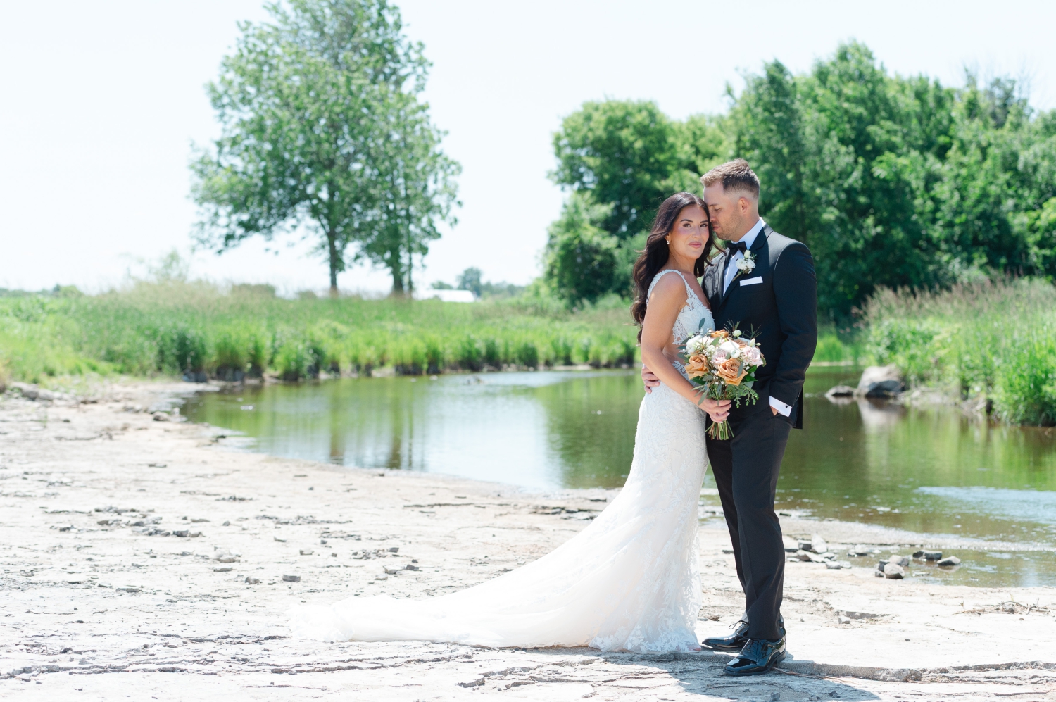 a photo of a bride and groom standing on the riverbank of the Ottawa outdoor wedding venue, Bleeks and Bergamot. Captured by Ottawa wedding photographer JEMMAN Photography