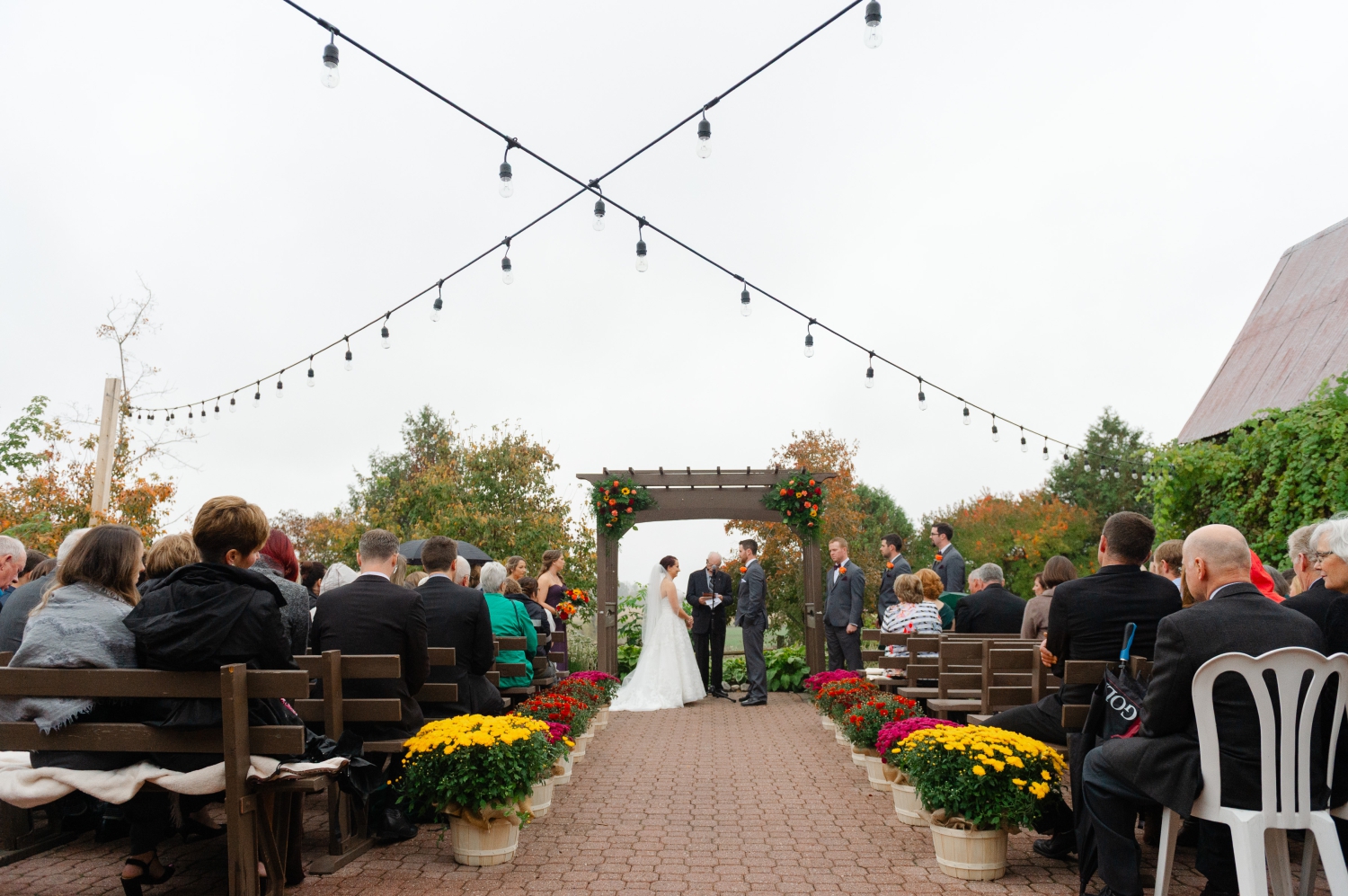 a sweeping photo of a bride and groom and their guests during their Ottawa outdoor wedding ceremony at Strathmere Estates. Captured by JEMMAN Photography