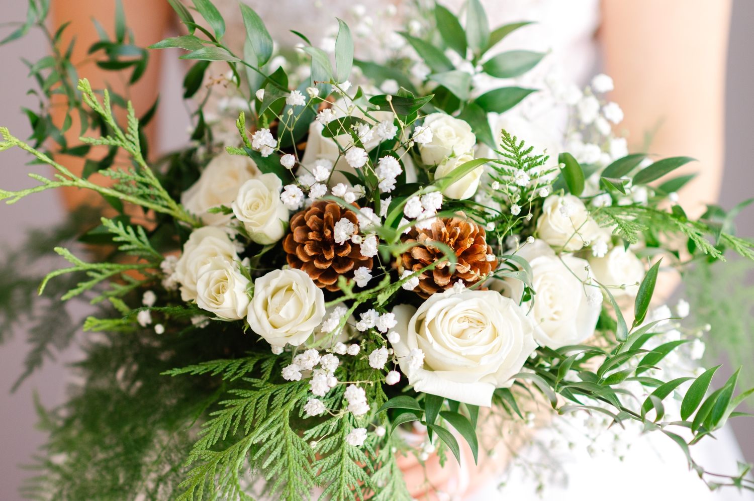 a closeup photo of a winter style wedding bouquet with white roses, pine cones and evergreens created by Ottawa wedding florist The Planted Arrow and captured by JEMMAN Photography