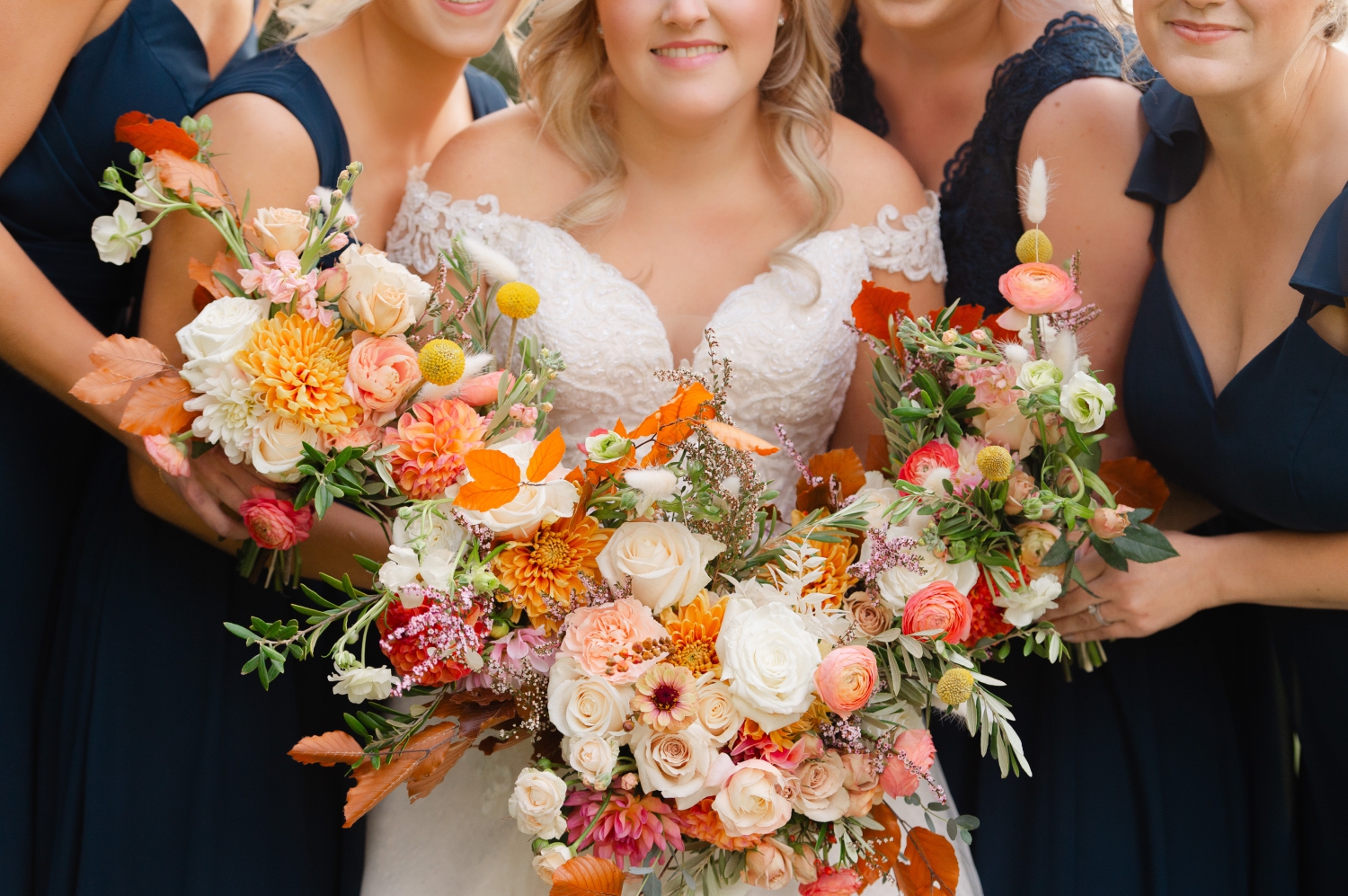 a closeup photo of a bride and bridesmaids in blue dresses holding orange coloured floral bouquets, created by Ottawa wedding florist, Riverwood Gardens. Captured by JEMMAN Photography