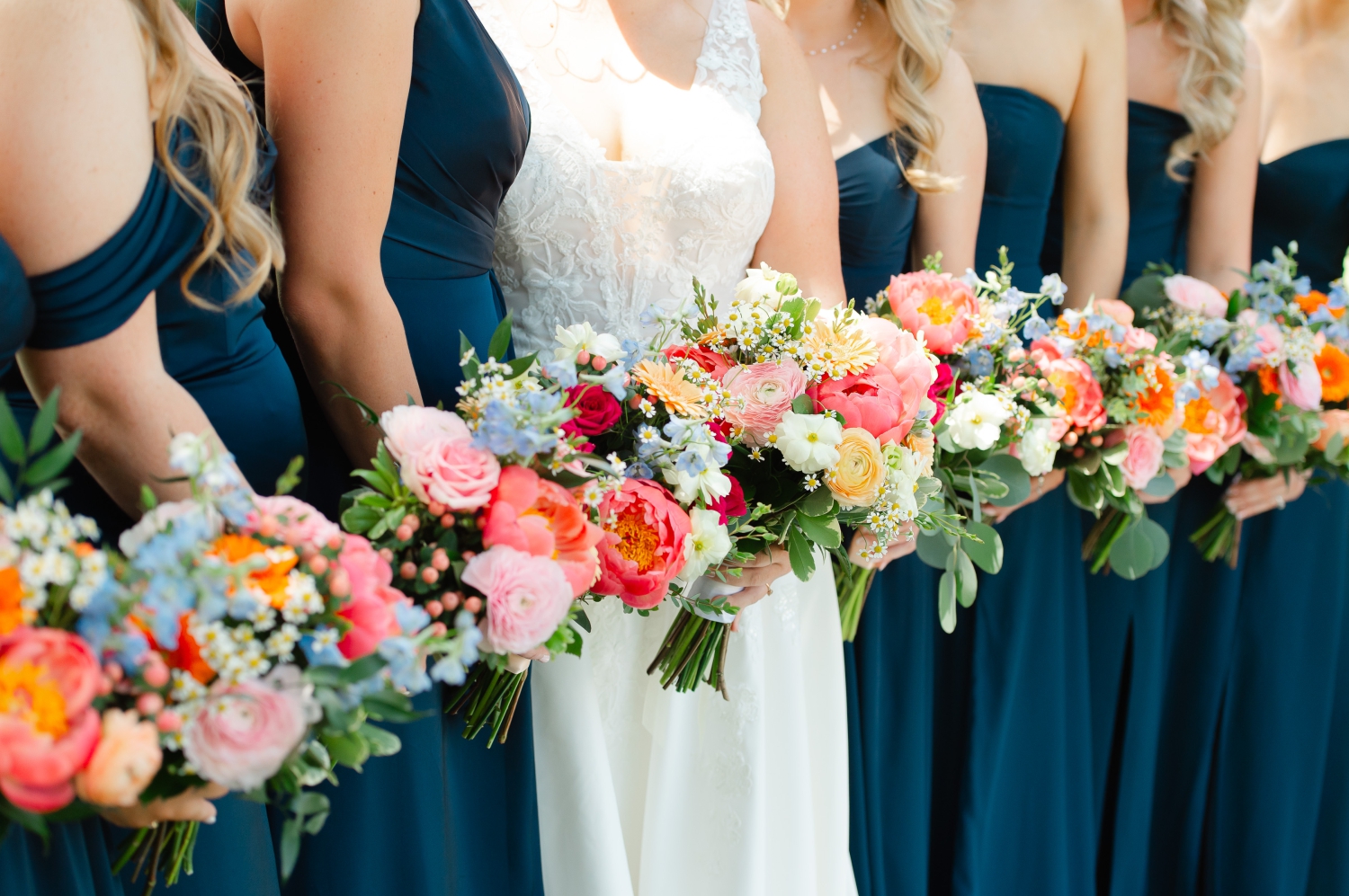 a closeup photo of brightly coloured Ottawa wedding florals held by a bride and her bridesmaids in blue gowns