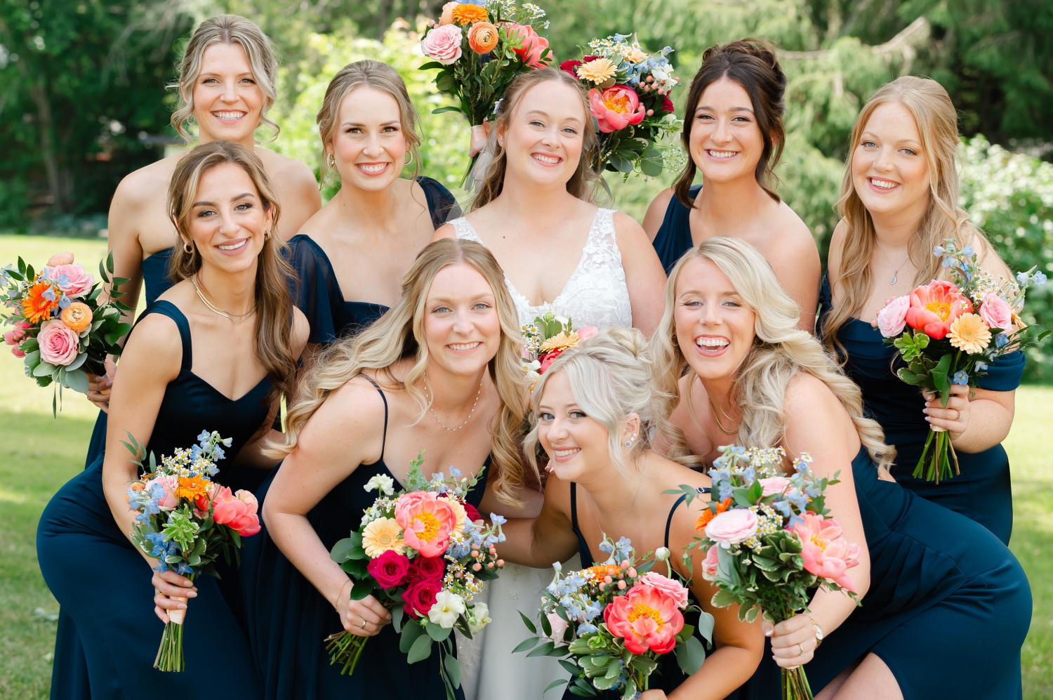 a photo of a bride and her bridesmaids in blue dresses holding brightly coloured wedding bouquets created by Ottawa wedding florist The Flower Shop Kemptville. Captured outdoors by JEMMAN Photography