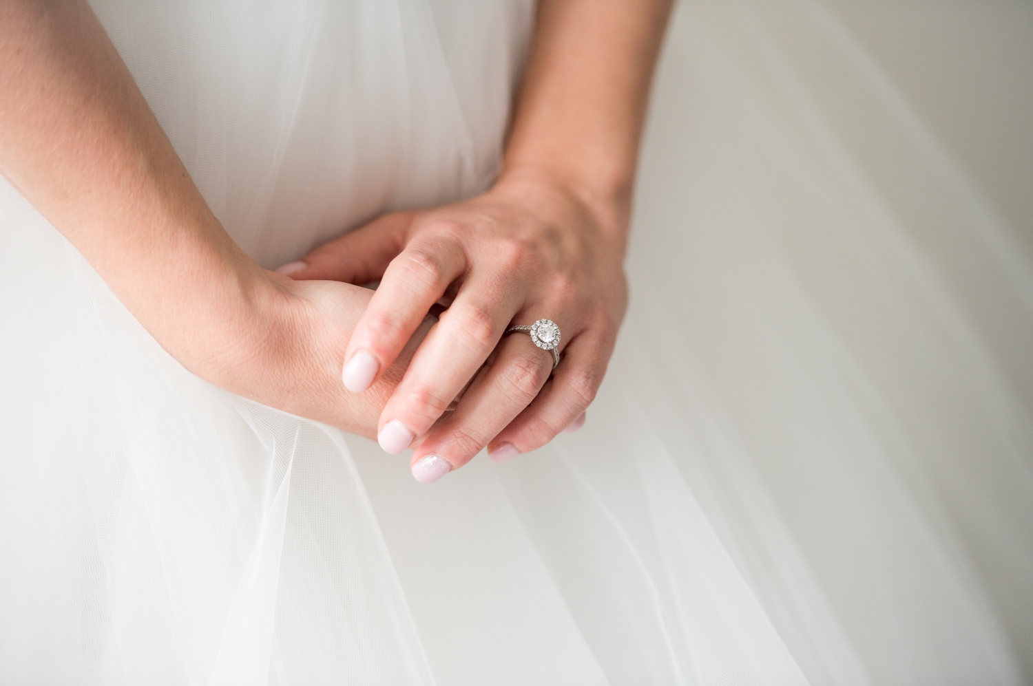 a photo of a bride clasping her hands in front of her wedding dress. The focus is on her beautiful diamond engagment ring. Captured on wedding day by JEMMAN Photography