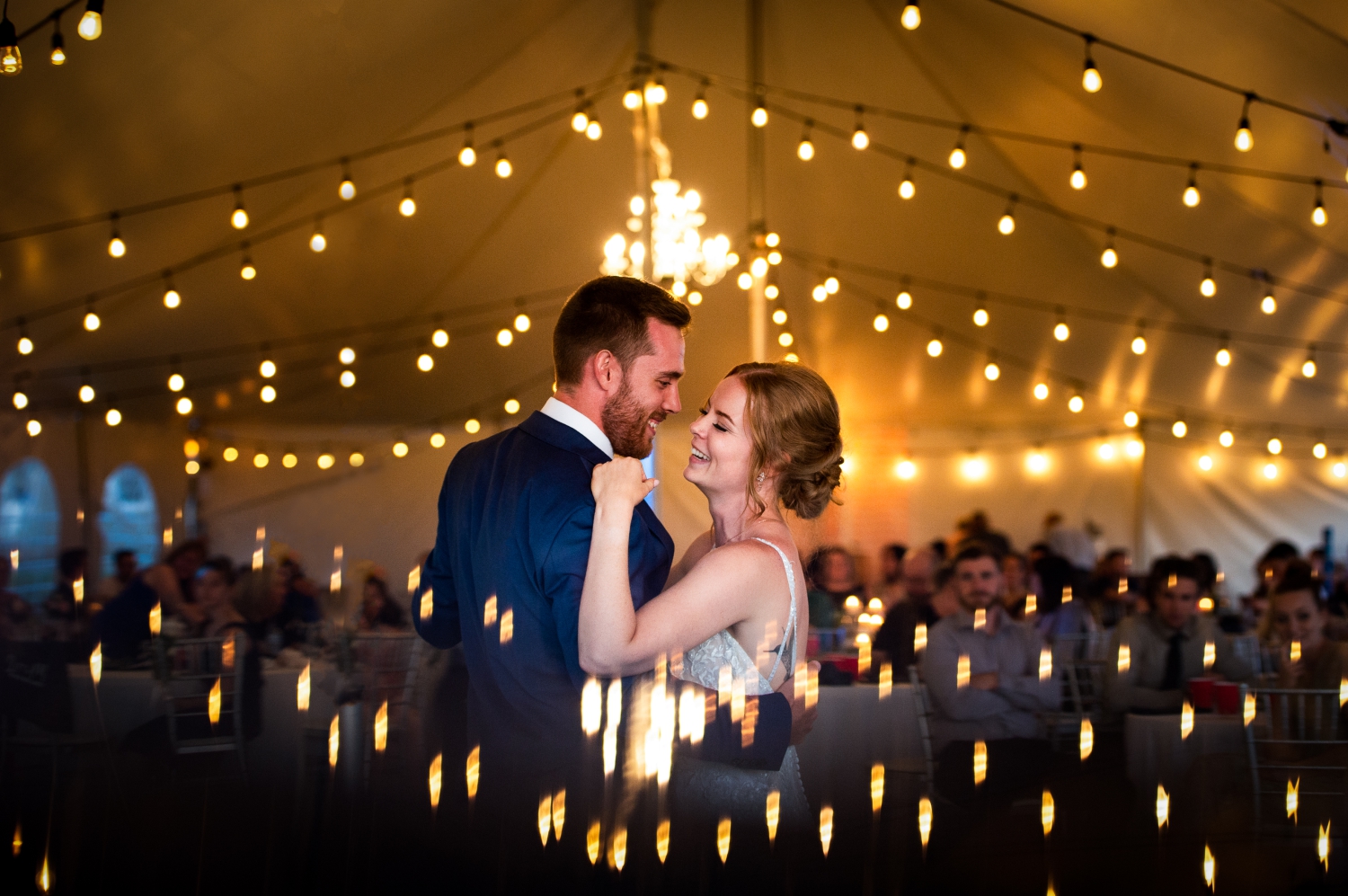 a bride laughing at her groom in a blue suit with twinkle lights around them during their first dance in Ottawa